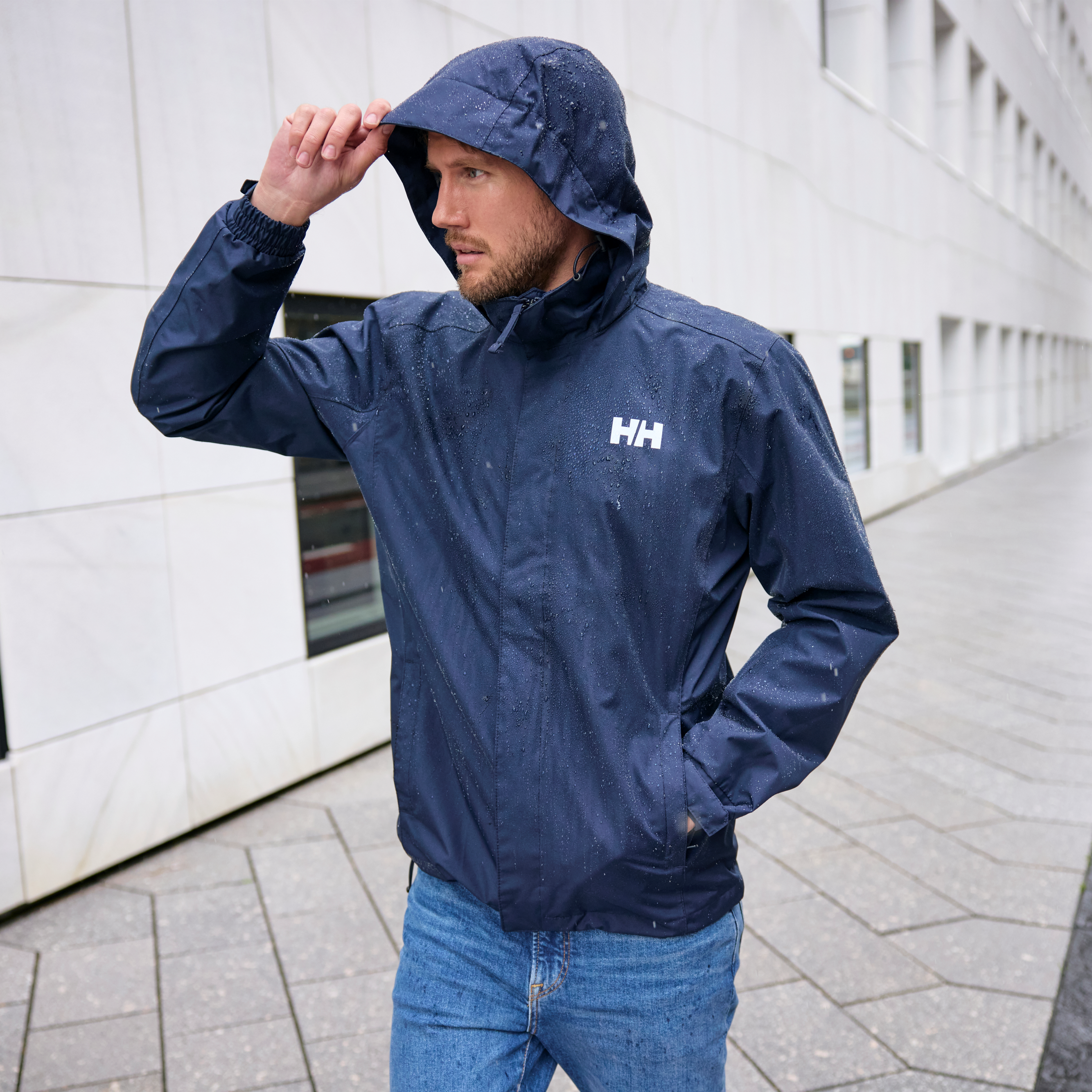 Man walking in a city in the rain wearing 62643 Helly Hansen Men's Dubliner Waterproof Rain Jacket Navy 597 with water droplets on the jacket