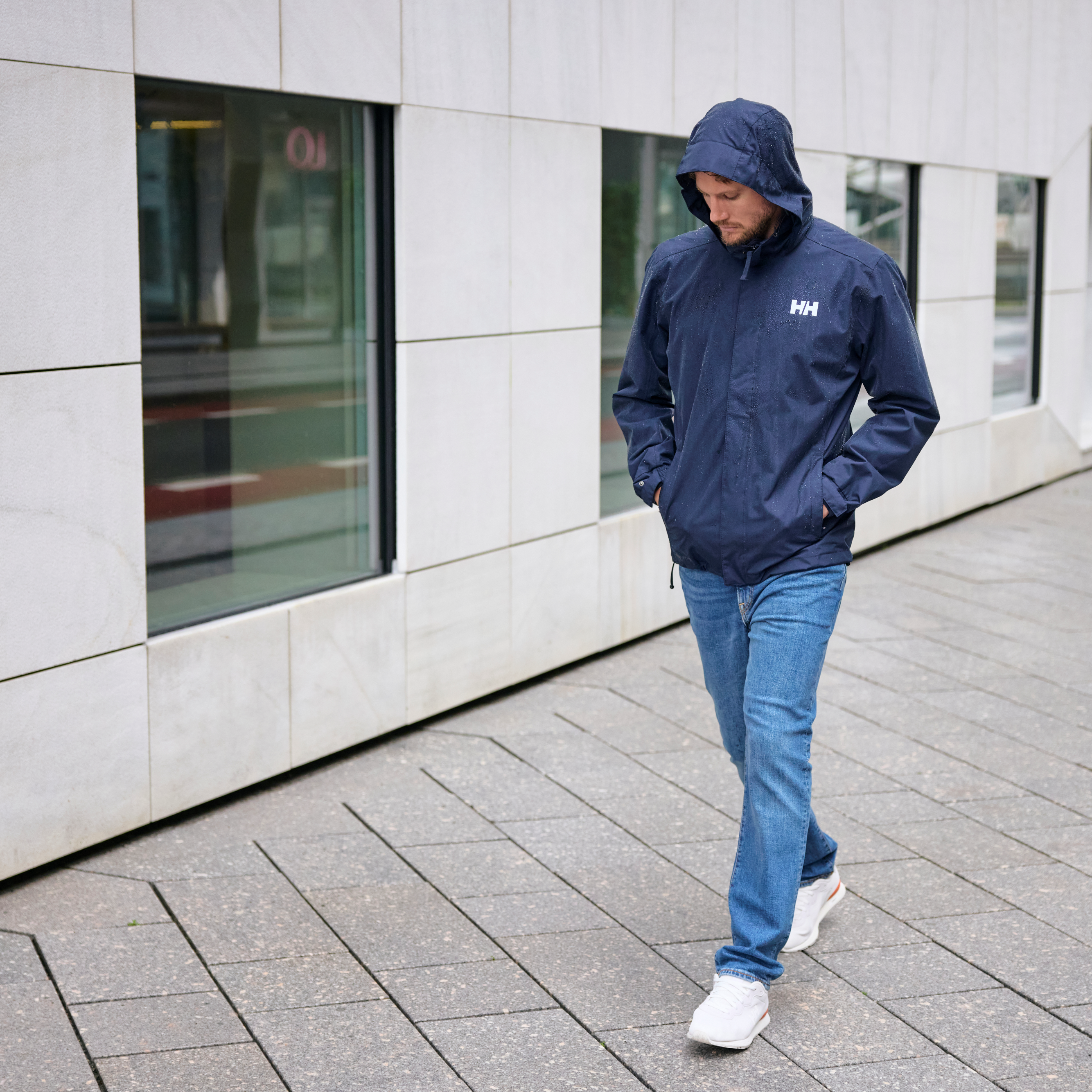Man walking in a city in the rain wearing 62643 Helly Hansen Men's Dubliner Waterproof Rain Jacket Navy 597 with water droplets on the jacket