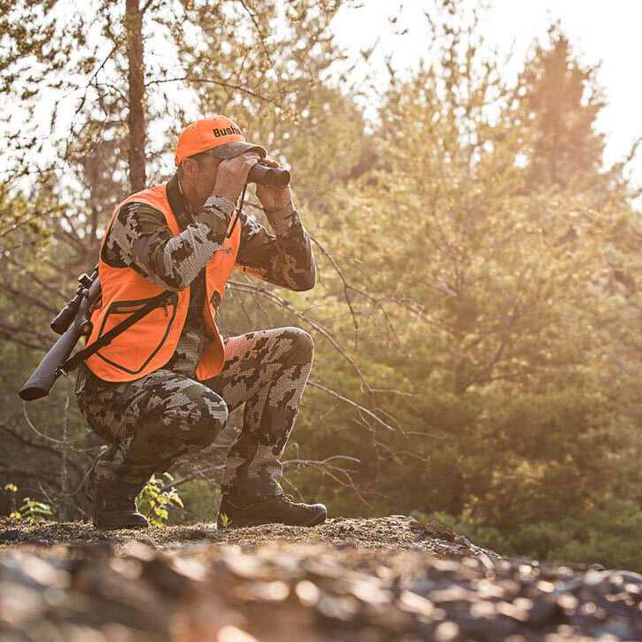 Hunter in camouflage and orange vest using Bushnell Powerview 2 Binoculars in a forest setting