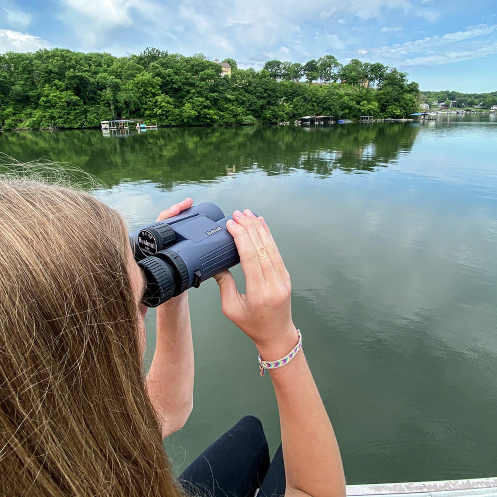 Woman using Bushnell H2O Aluminium Roof Binoculars to look across a lake at trees