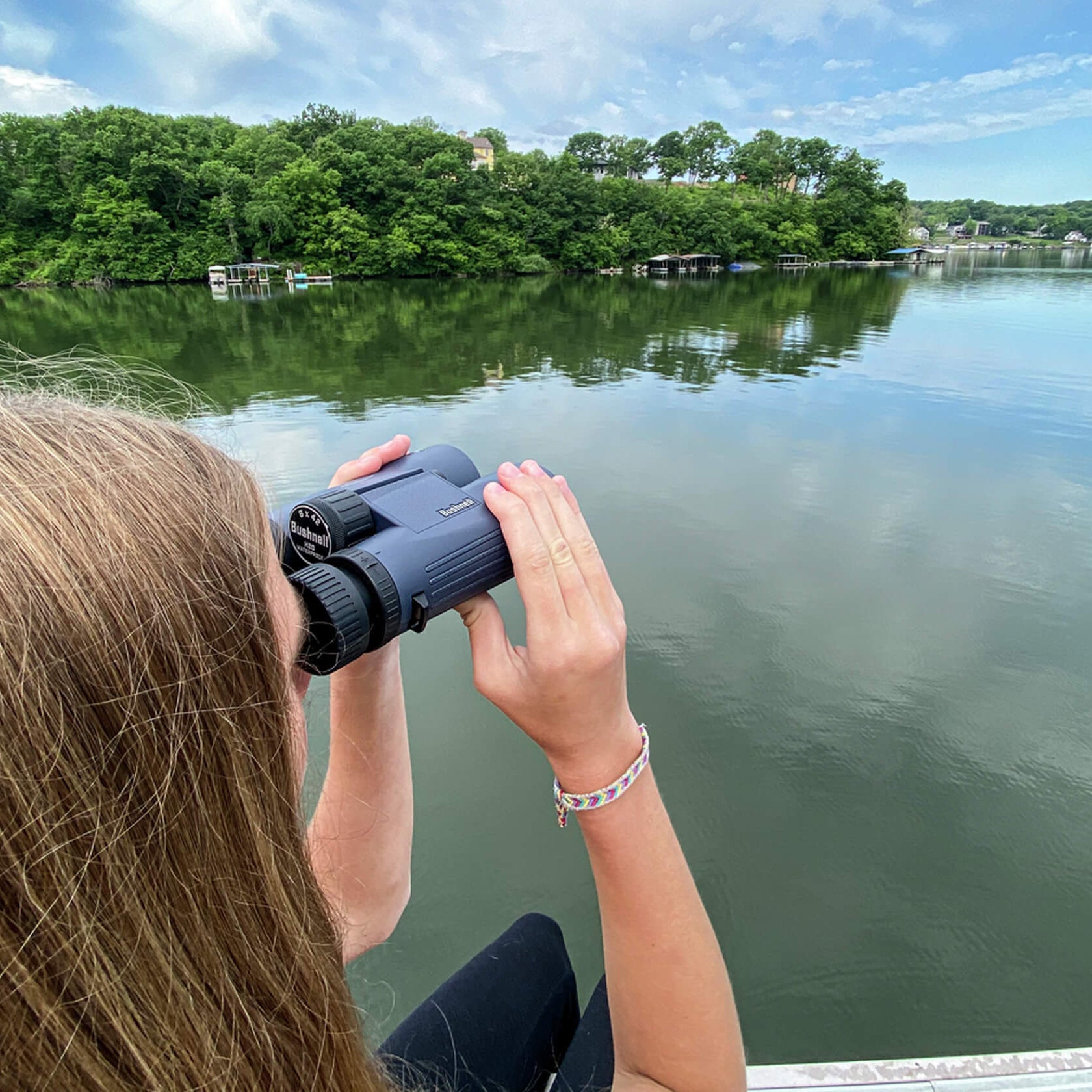 Woman using Bushnell H2O Waterproof Binoculars to look at a lake with trees and houses in the background