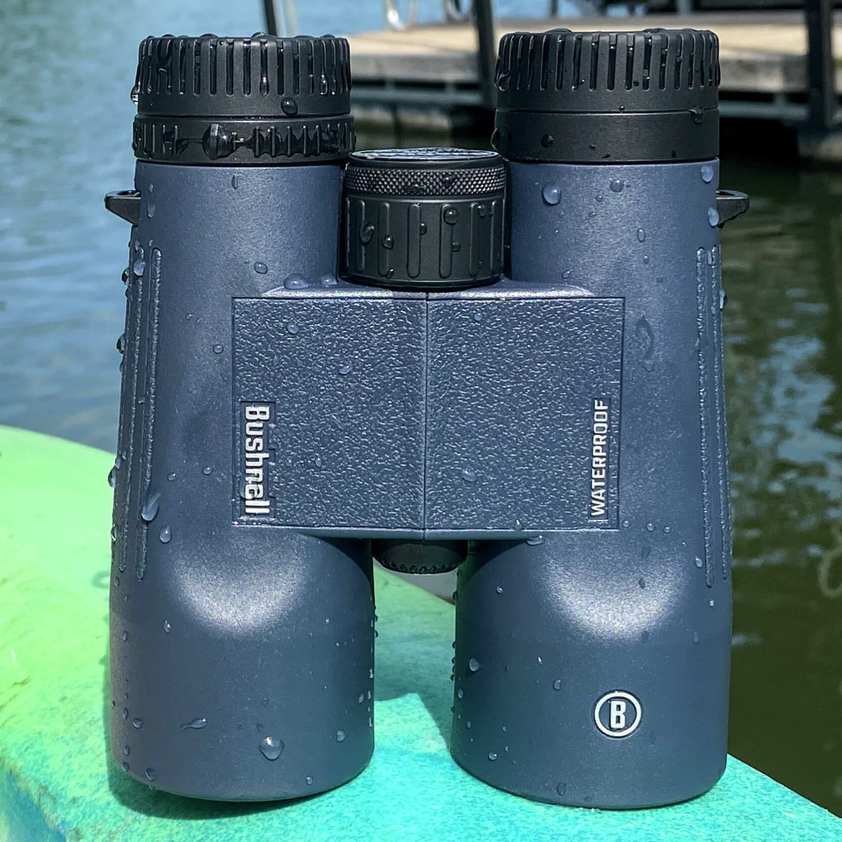 Bushnell H2O Waterproof Binoculars with water drops on it sitting on top of a kayak by the water