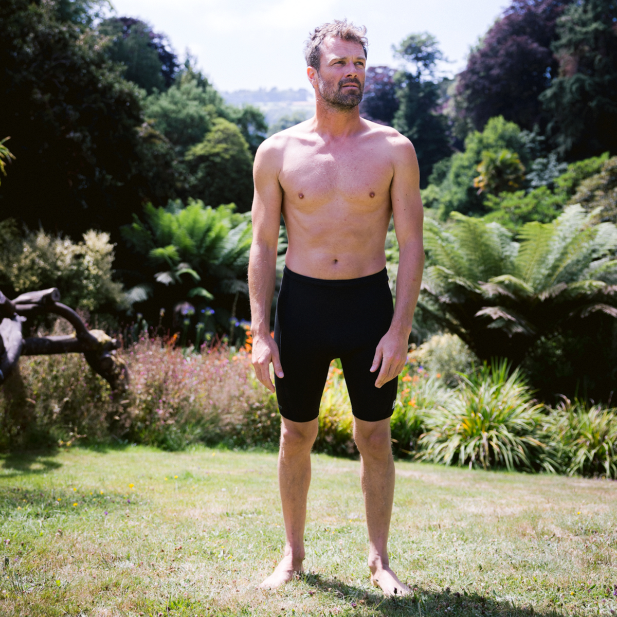 Man wearing C-Skins Men's NuWave Legend 2 2mm Neoprene Shorts Black C-NLE22SH standing in the grass