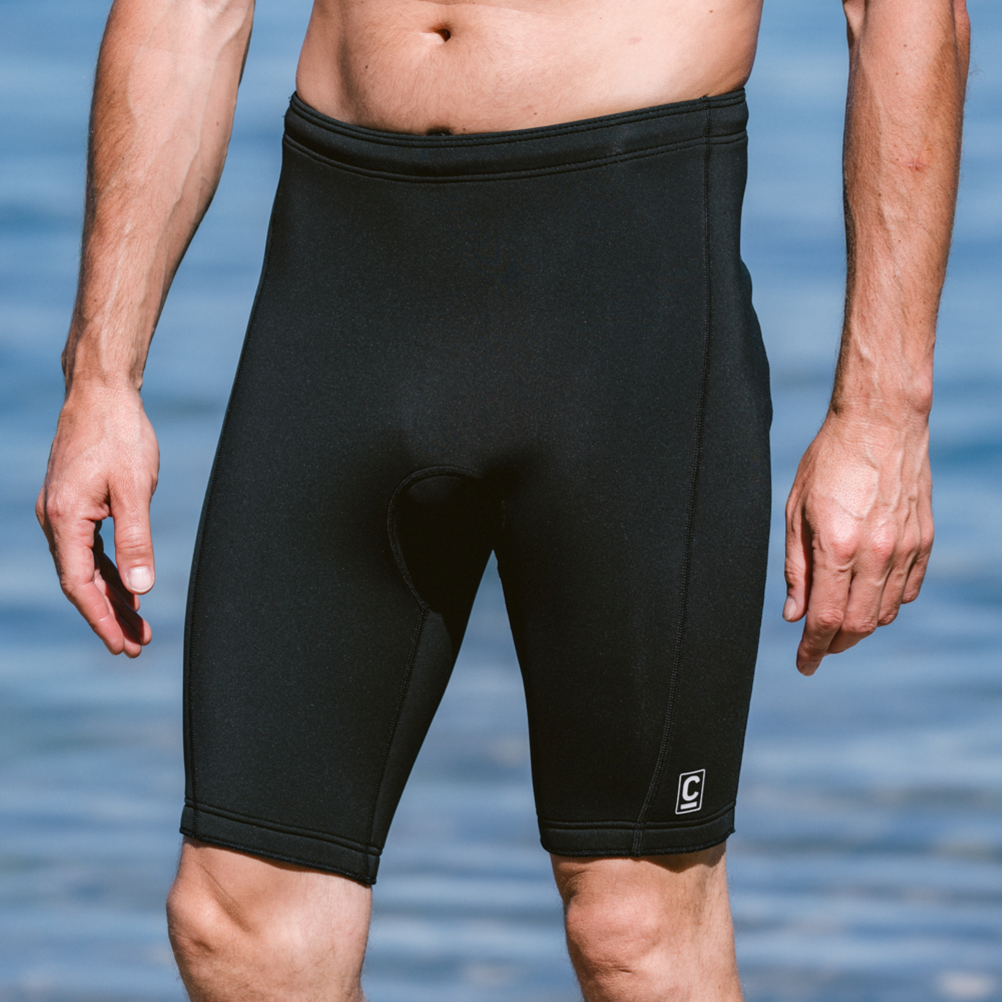 Close up of a man wearing C-Skins Men's NuWave Legend 2 2mm Neoprene Shorts Black C-NLE22SH, sea background