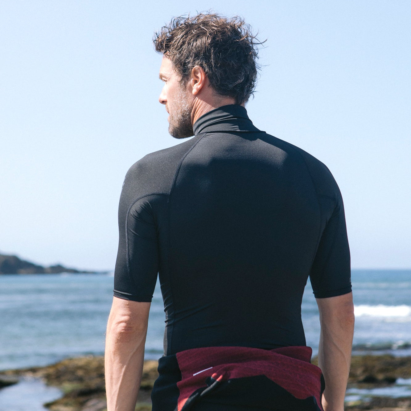 Man wearing C-Skins Men's NuWave Rash X UPF50 Short Sleeve Rash Vest Black C-NLYSSMT on the beach