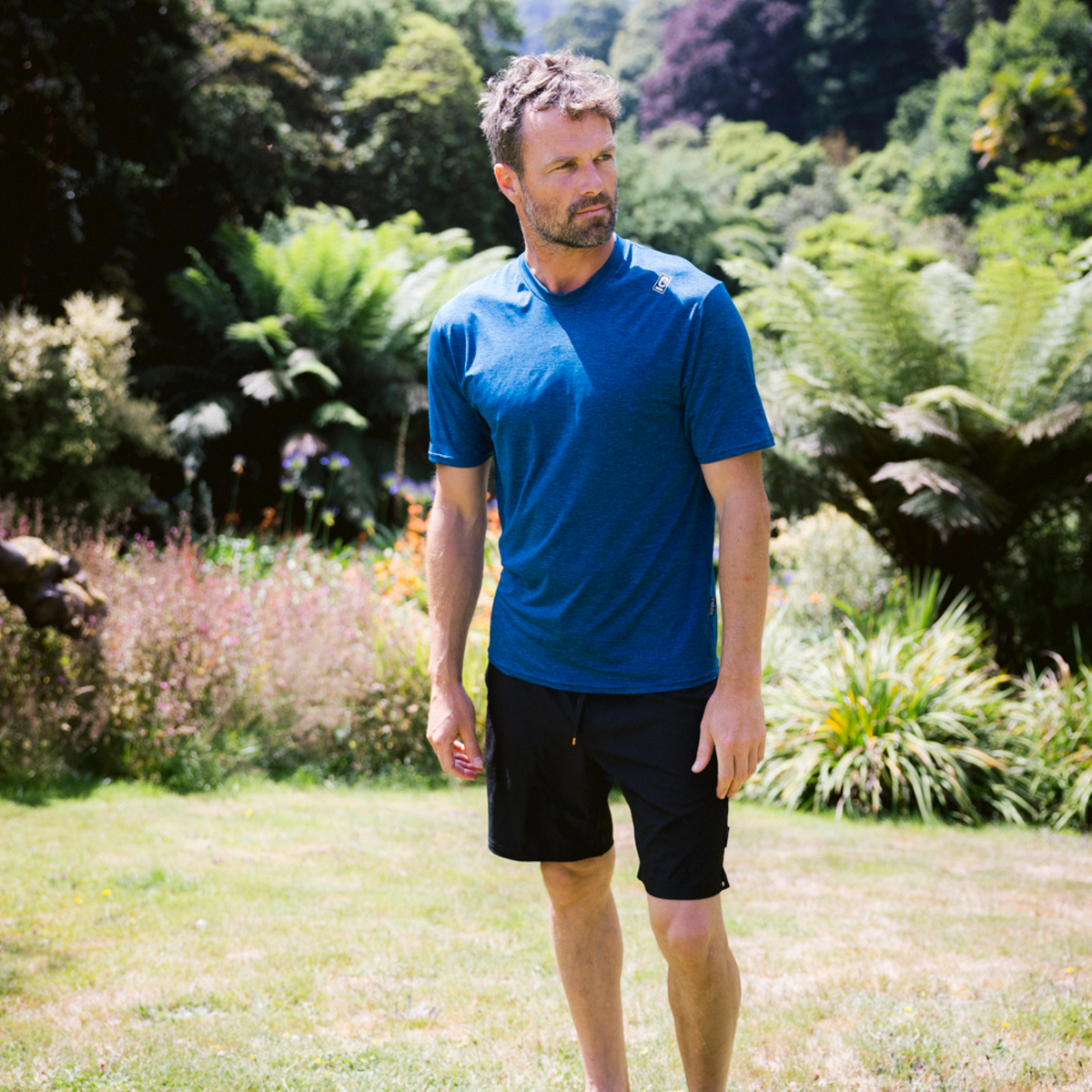 Man wearing C-Skins Men's NuWave UV UPF50 Short Sleeve Surf Tee Deep Blue C-NLYSURFM with a green grassy background