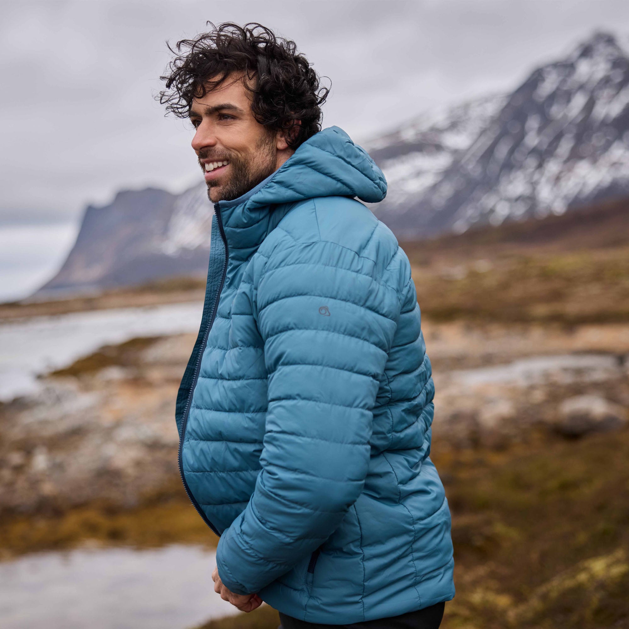 Man zipping up a Craghoppers Men's Complite IX Hooded Insulated Jacket Winter Storm 1Y0 CMN323 with a blurred mountain background