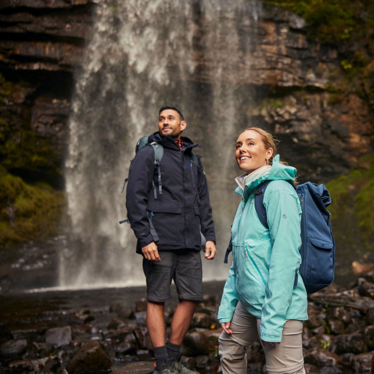 Three people in outdoor gear standing in front of a waterfall. Man at the back wearing Craghoppers Men's Lorton II Waterproof Jacket Dark Navy 3G3 CMW831