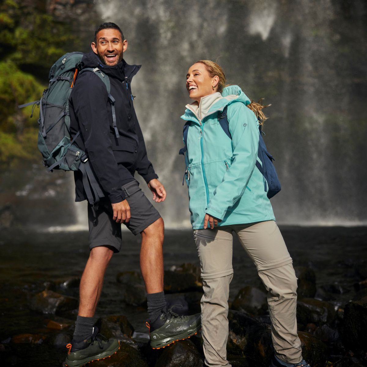 Two people hiking in front of a waterfall. Man wearing Craghoppers Men's Lorton II Waterproof Jacket Dark Navy 3G3 CMW831
