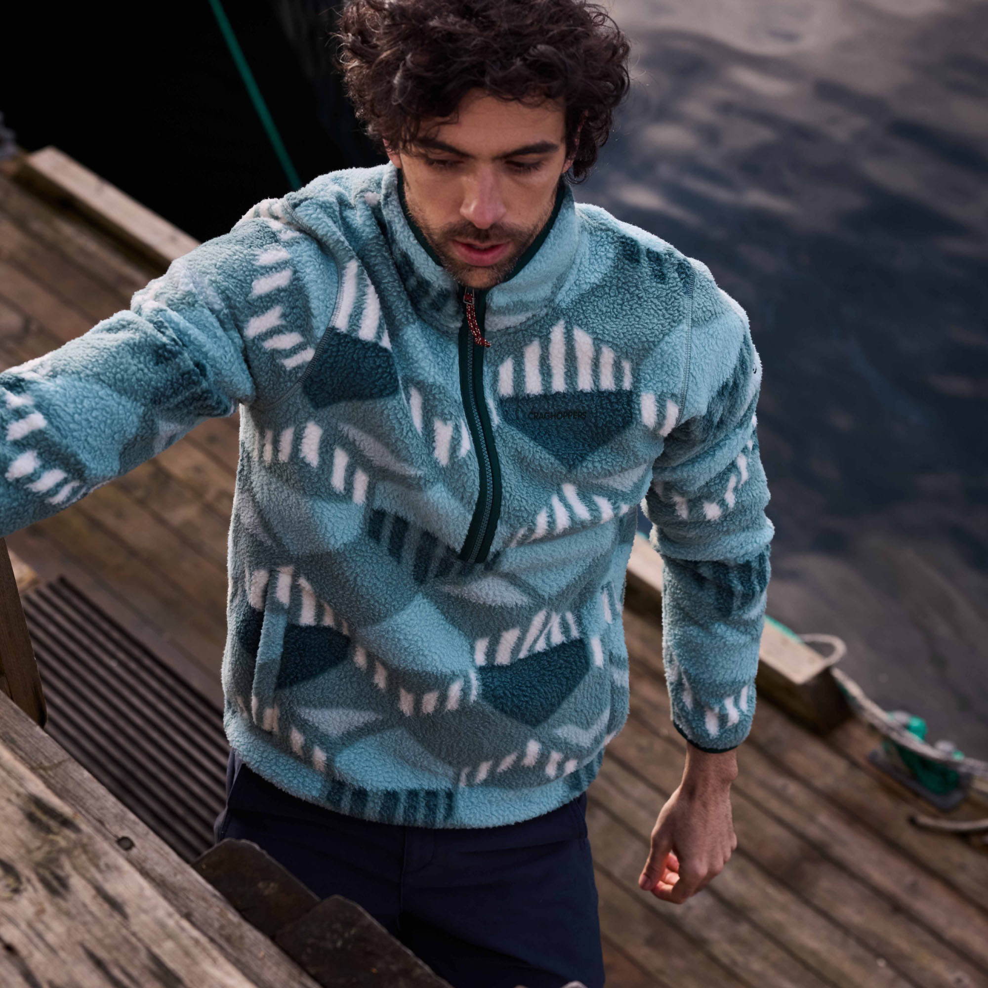 Man wearing a Craghoppers Men's Tatton Half Zip Fleece Top Green Ridge 1YU CMA1429 standing on a wooden pier by the water