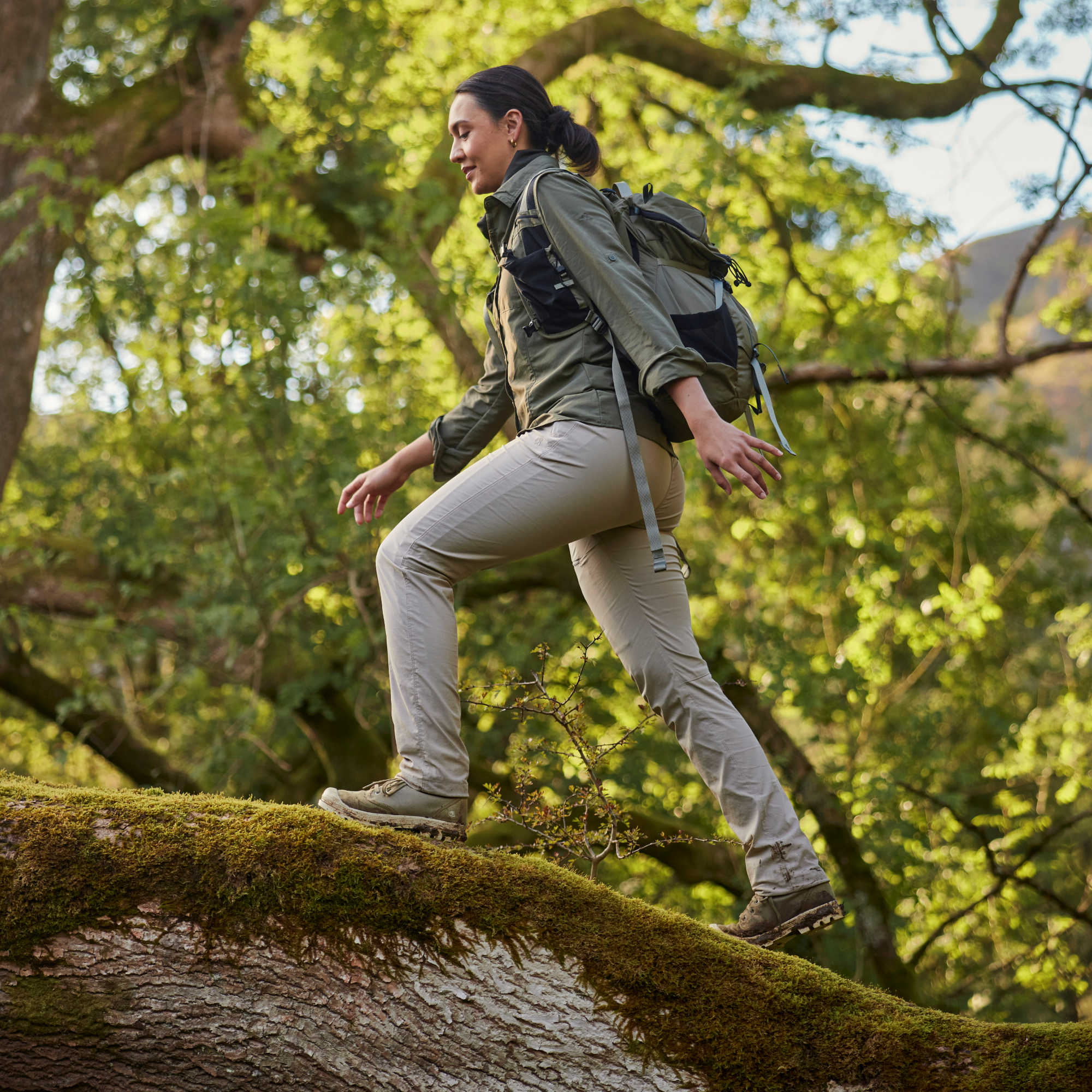 Woman hiking on fallen tree wearing Craghoppers Women's Nosilife Pro III Insect Repellent UPF50 Trousers Soft Mushroom KD7 CWJ1373