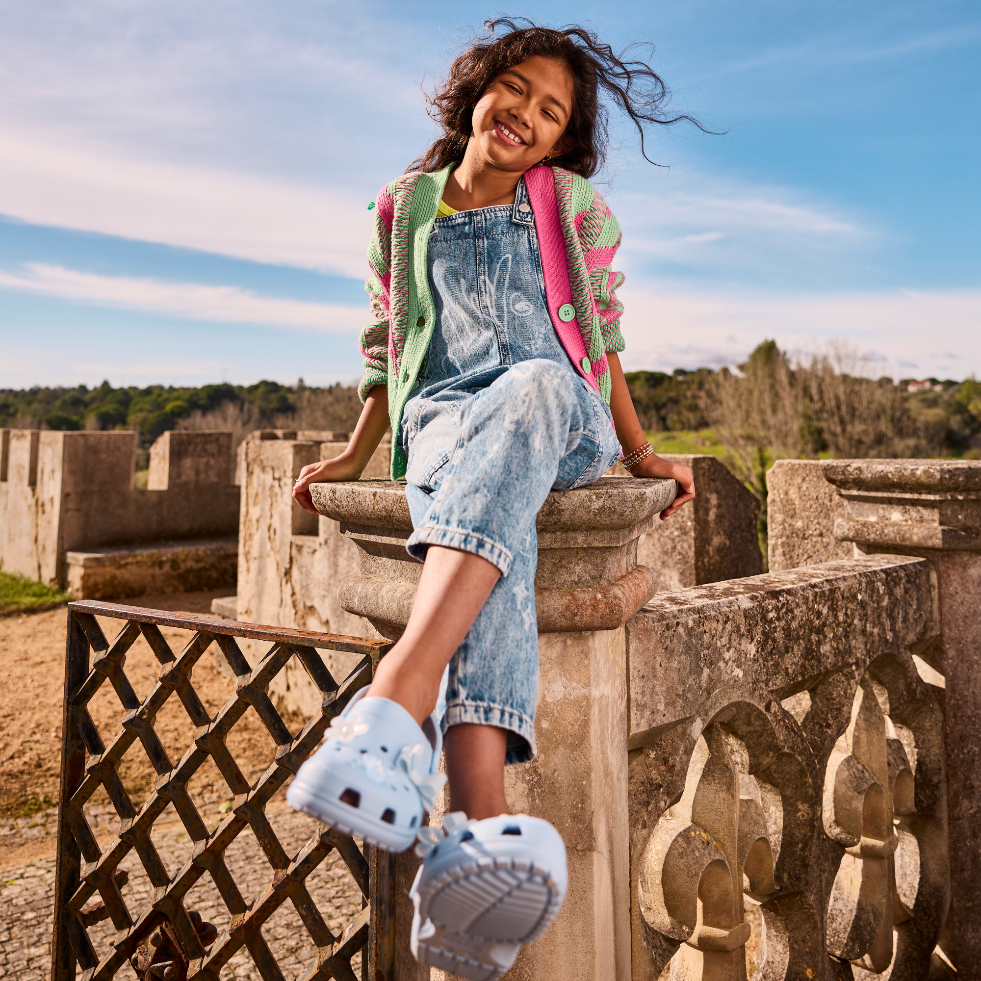 Young girl sitting on a pillar wearing Crocs Classic Clogs Junior Blue Calcite 4NS 206991