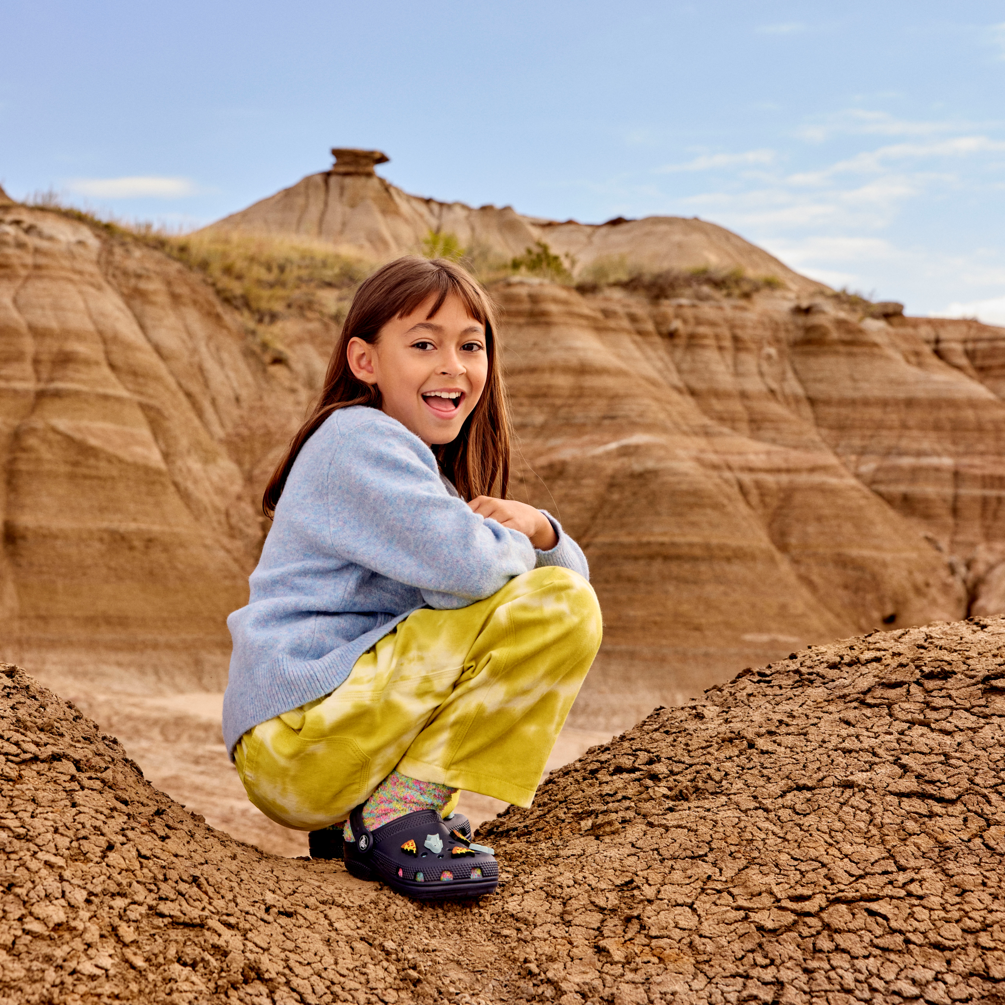 Child sitting on a rocky hill with a blue sky and clouds in the background wearing Crocs Classic Clogs Junior Navy 410 206991