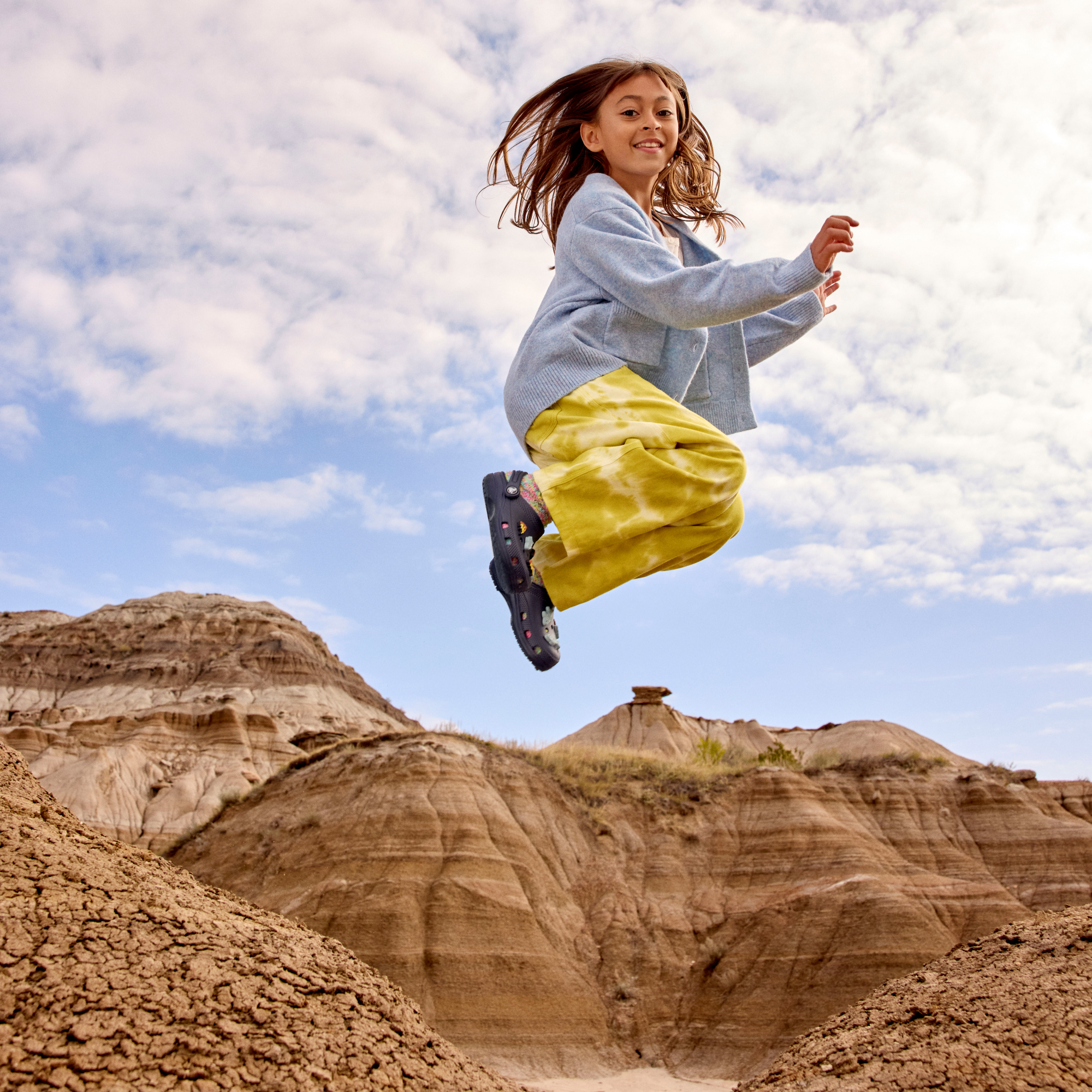 Young girl wearing Crocs Classic Clogs Junior Navy 410 206991 jumping in the air in a desert setting