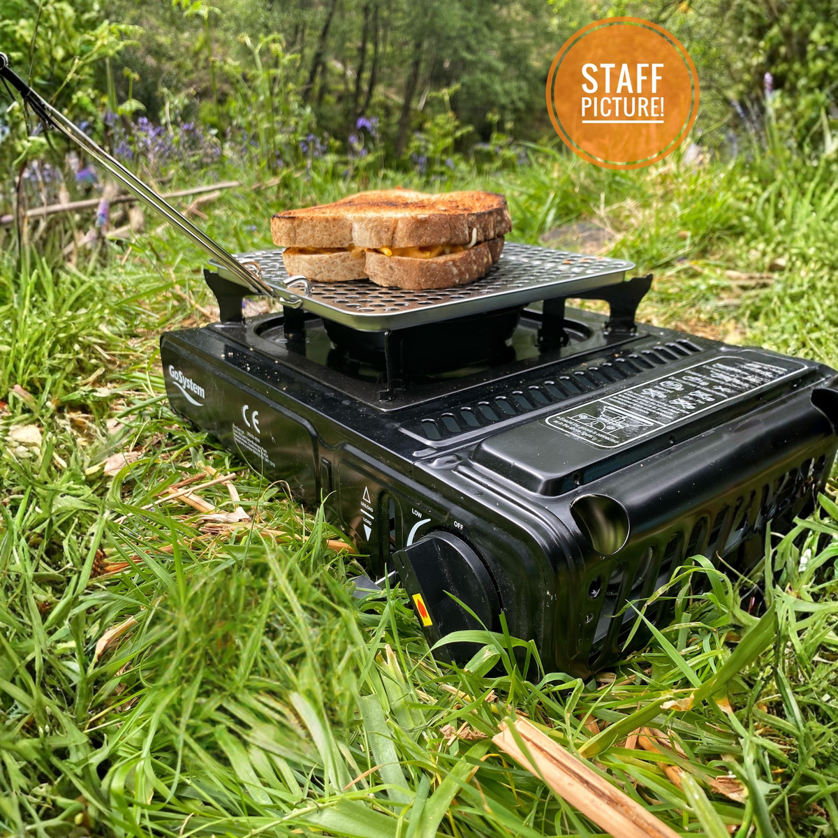 Go System Dynasty Compact Gas Camping Cooker II TM-GS2290 sitting on grass outside with bread toasting on a toasting plate
