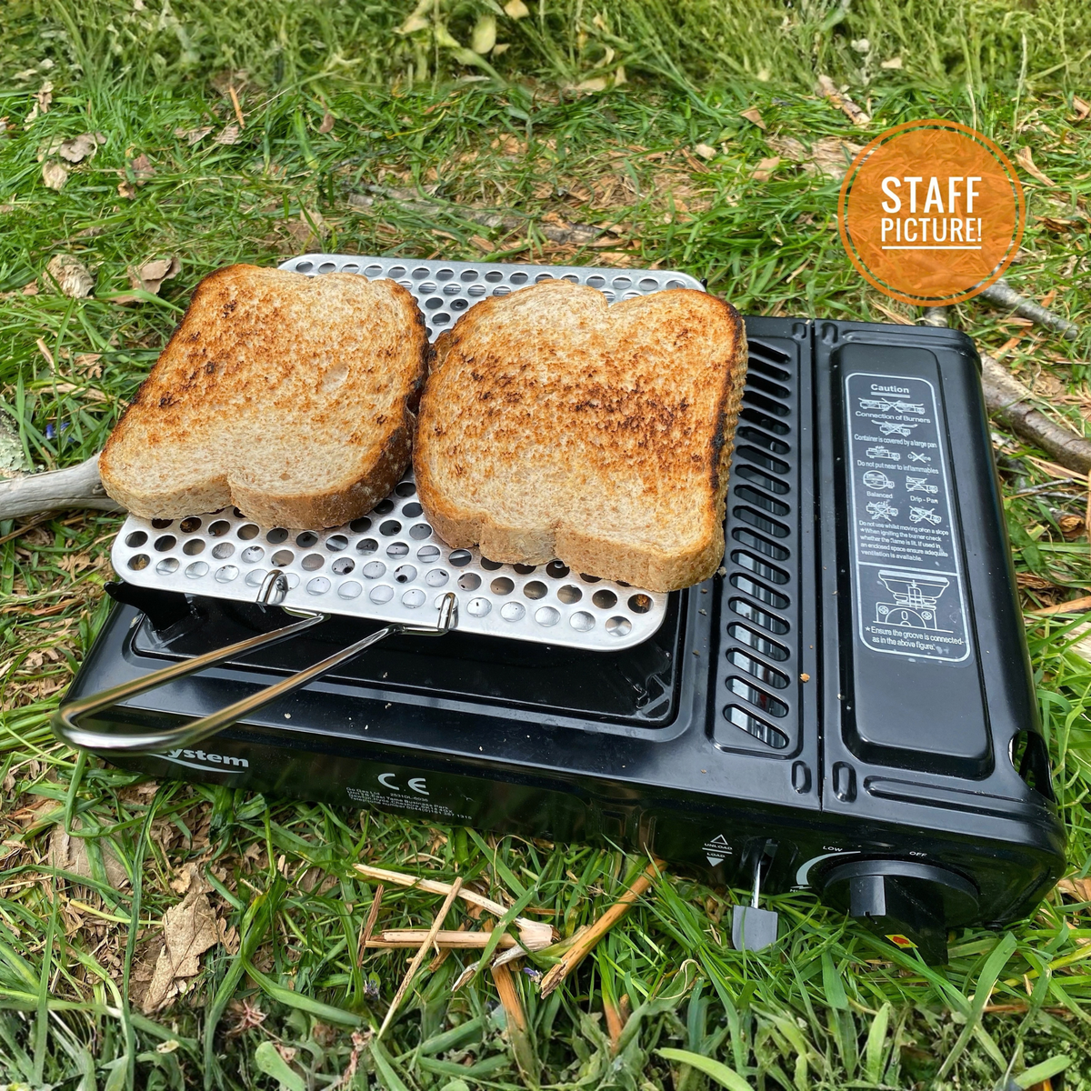 Bread toasting on a toasting plate on top of the Go System Dynasty Compact Gas Camping Cooker II TM-GS2290, sitting on the grass otuside