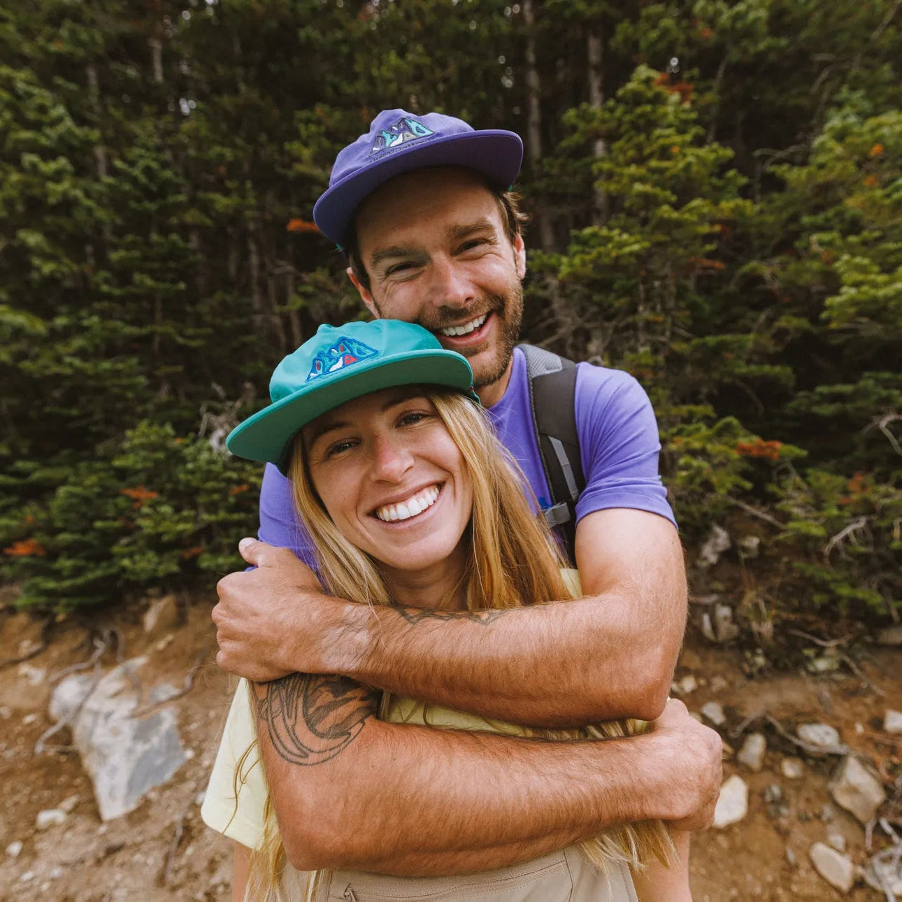 Two people hugging outdoors with a forest background. Both wearing Helly Hansen Unisex Awe Summer Cap