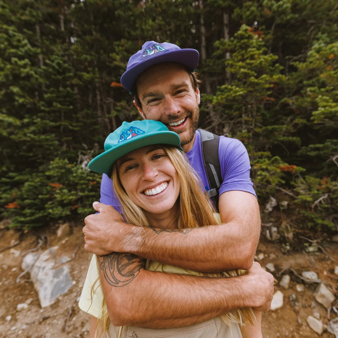 Two people hugging outdoors with a forest background. Both wearing Helly Hansen Unisex Awe Summer Cap