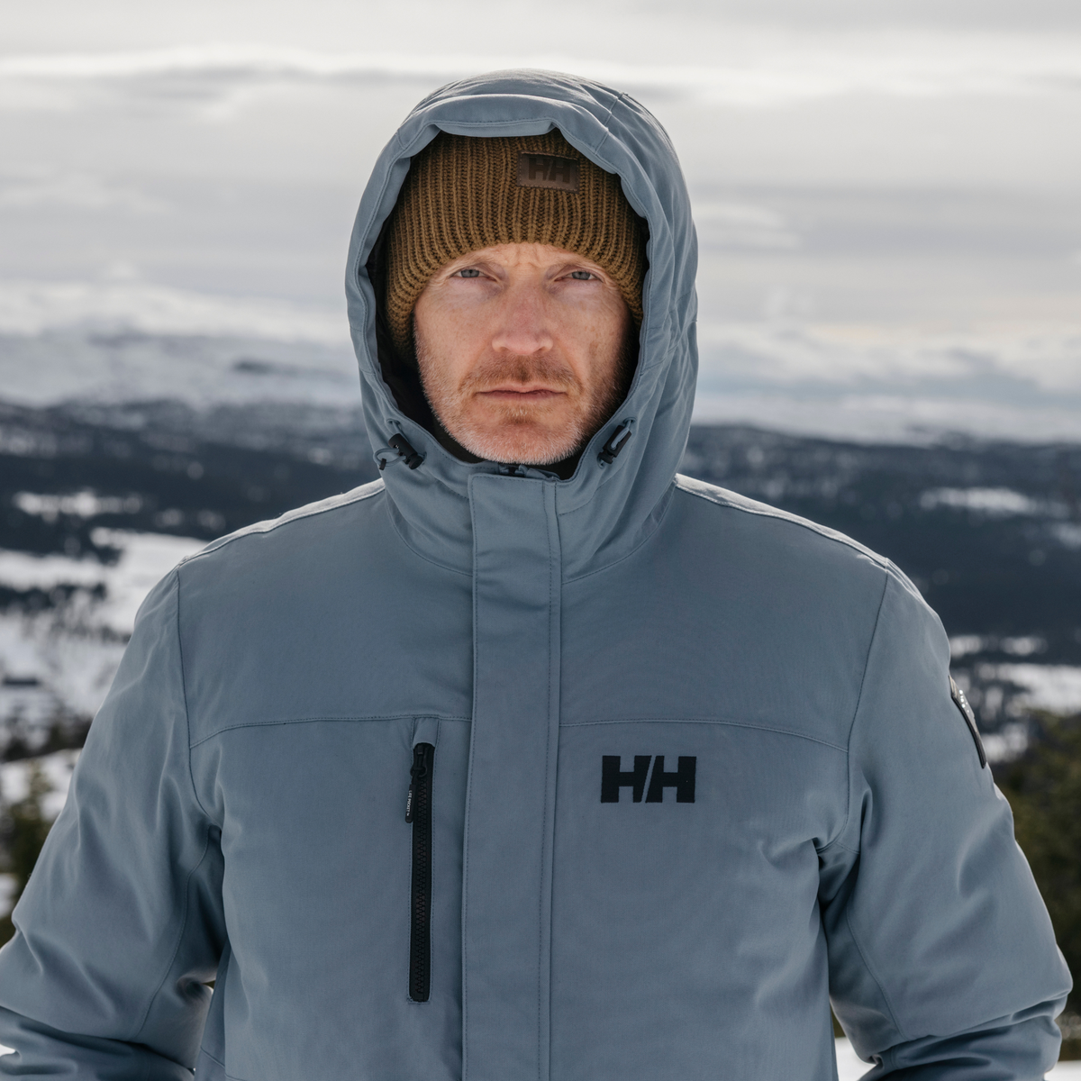 Person wearing a blue Helly Hansen jacket with a Helly Hansen Unisex HH Rib Beanie Hat Sepia 718 54020 in a snowy landscape