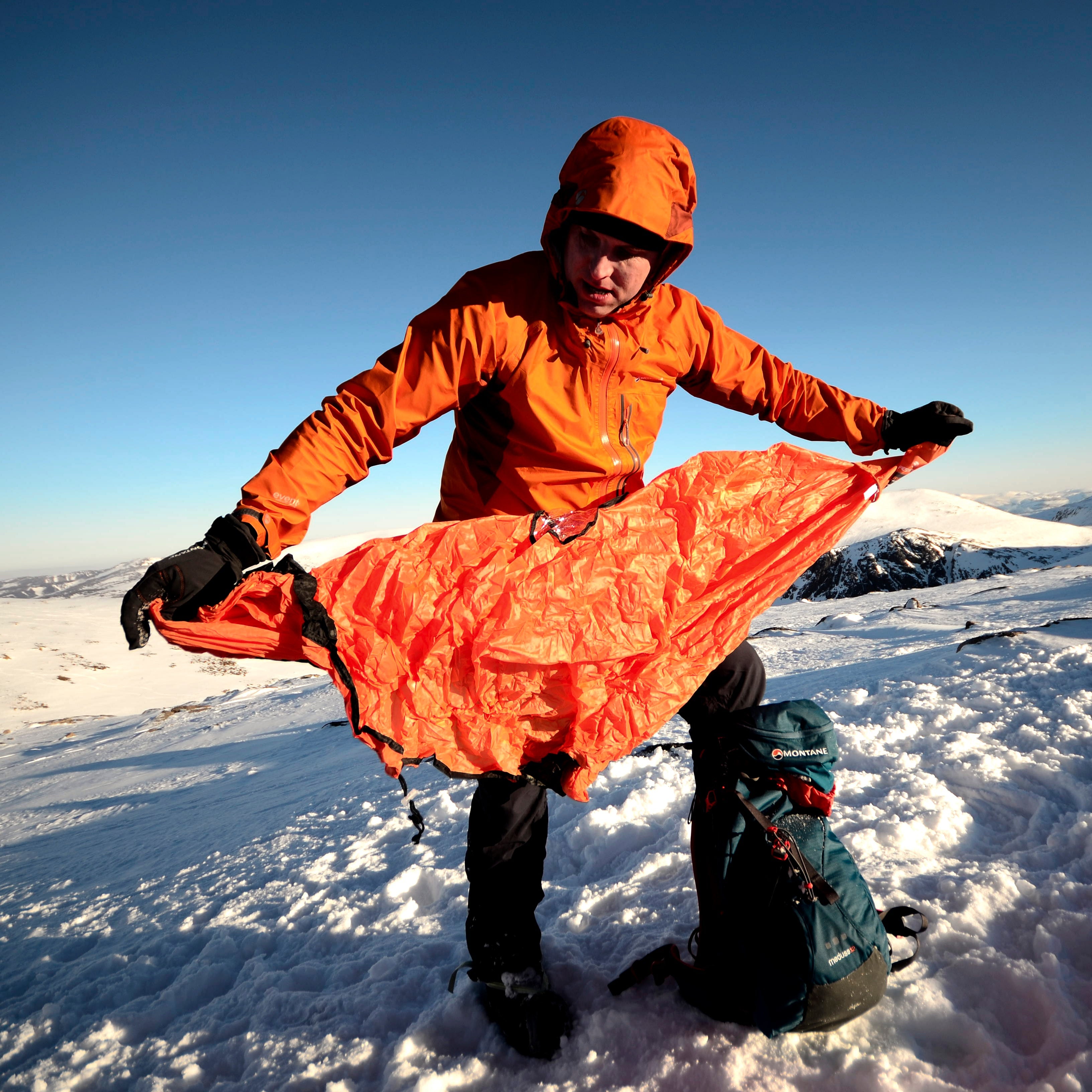Person in orange jacket setting up a Lifesystems Survival Shelter 2 People Orange 42311 on a snowy landscape