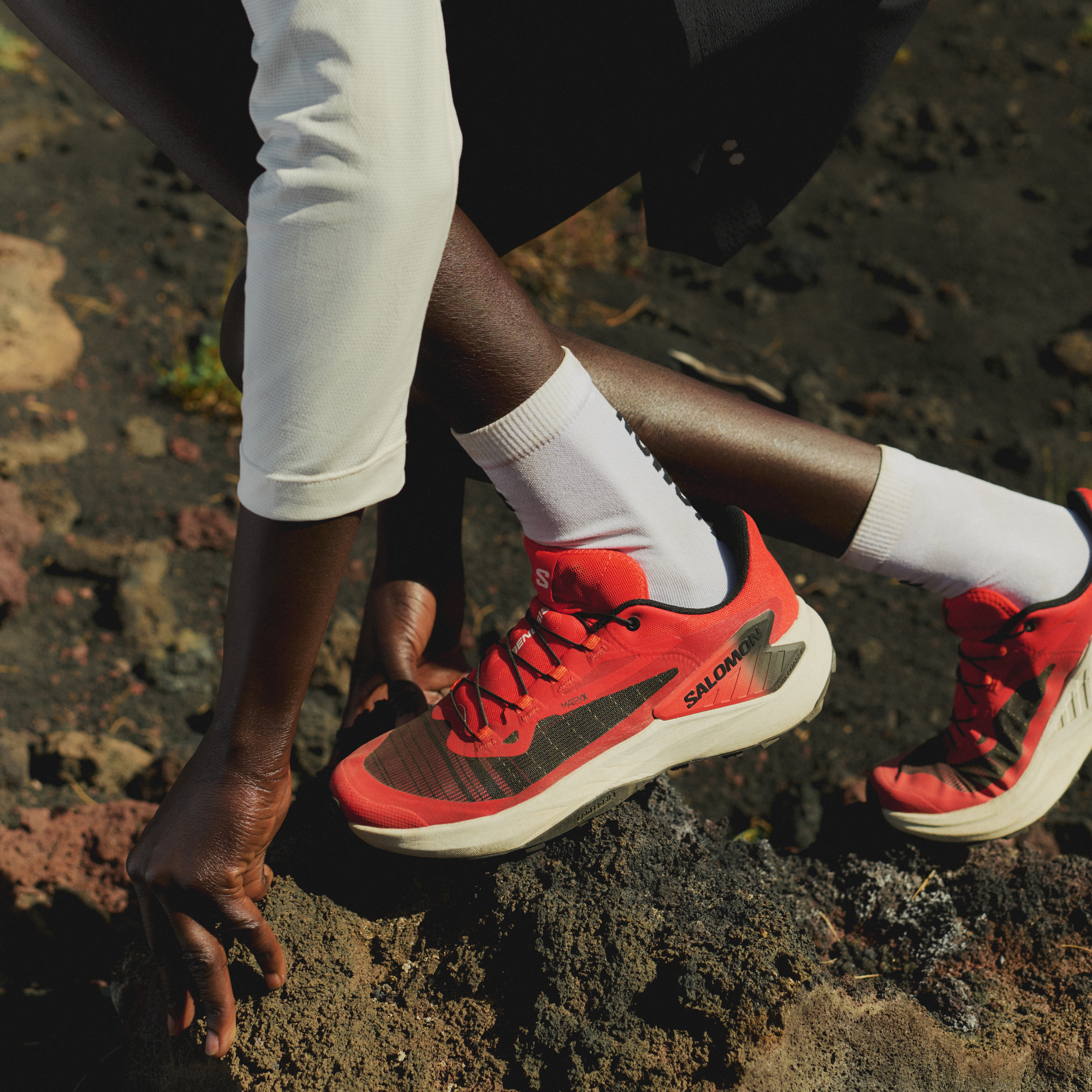 Person wearing Salomon Men's Genesis Trail Running Shoes Fiery Red Lava Falls Black L49226500 on a rocky surface