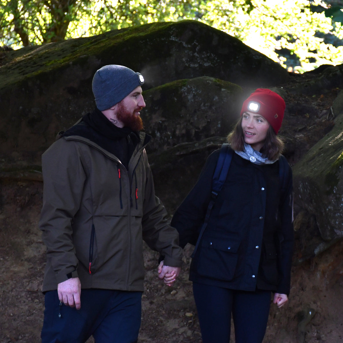 Two people walking in a forested area with large rocks and trees. Man wearing Six Peaks Unisex LED Lighted Beanie Hat Grey SIH0004