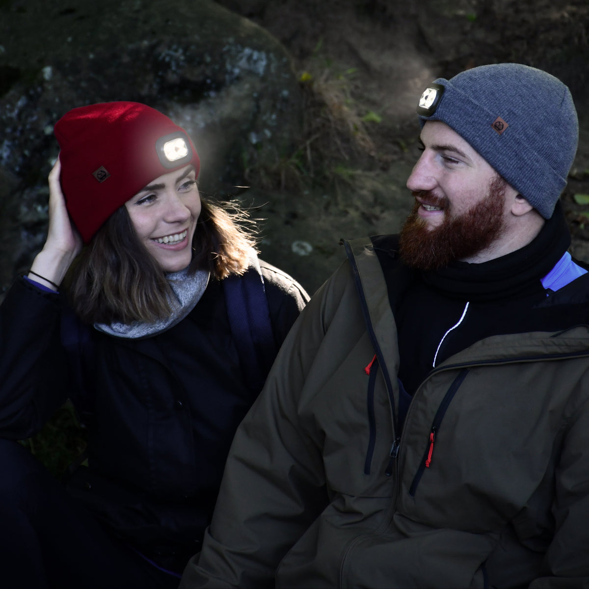 Two people in outdoor clothing in a dark forest setting. Man wearing Six Peaks Unisex LED Lighted Beanie Hat Grey SIH0004