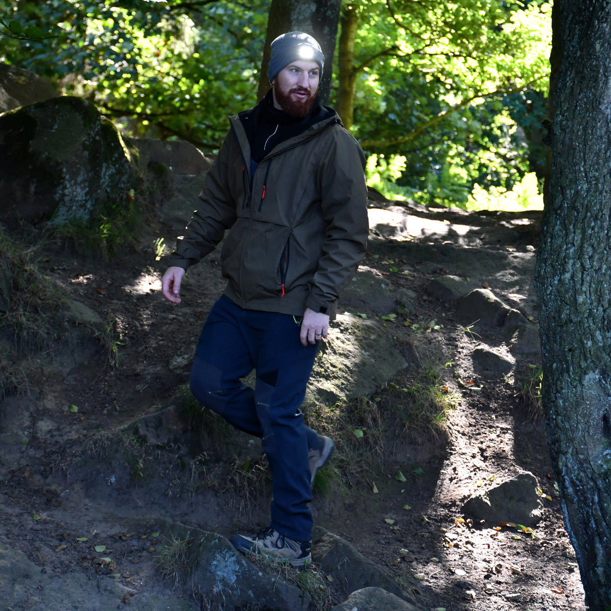 Person standing on a rocky path in a forest wearing Six Peaks Unisex LED Lighted Beanie Hat Grey SIH0004