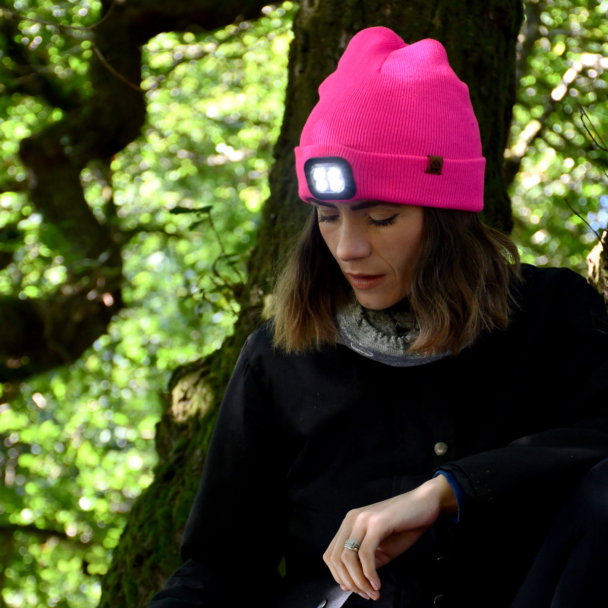 Person wearing a Six Peaks Unisex LED Lighted Beanie Hat Pink SIH0004 sitting outdoors in a forest.