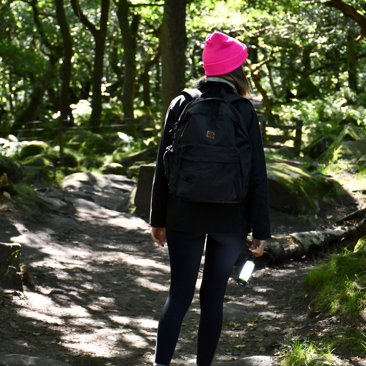 Person walking on a forest path wearing a Six Peaks Unisex LED Lighted Beanie Hat Pink SIH0004 and black backpack.