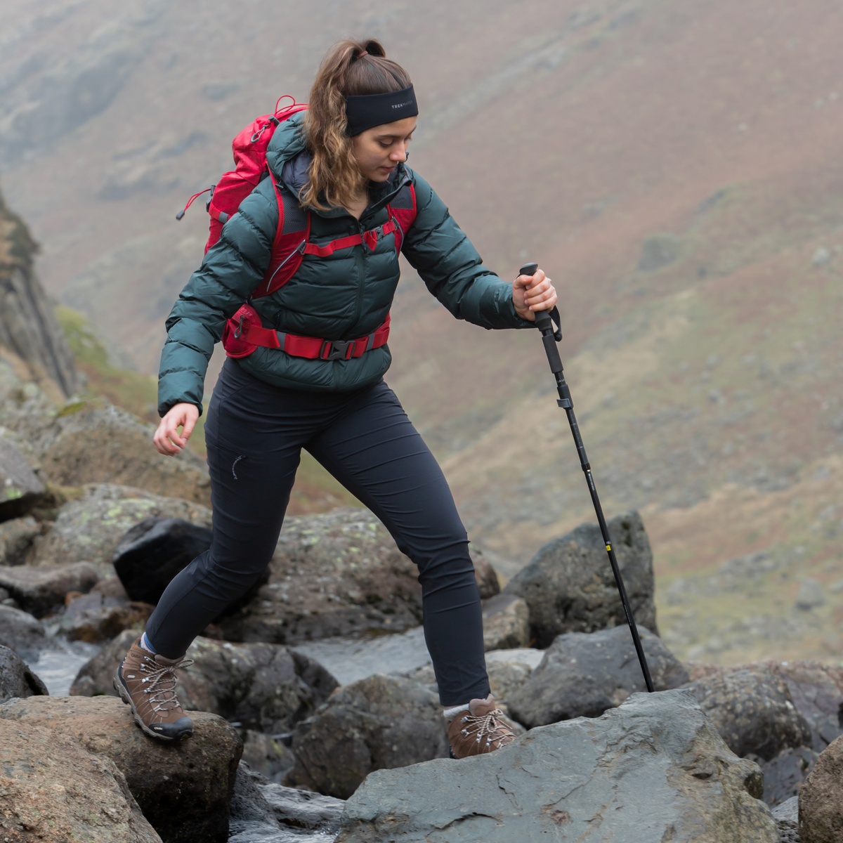 Person hiking on rocky terrain with a backpack and Trekmates Fold Lock Hiking Pole Black TM-008701