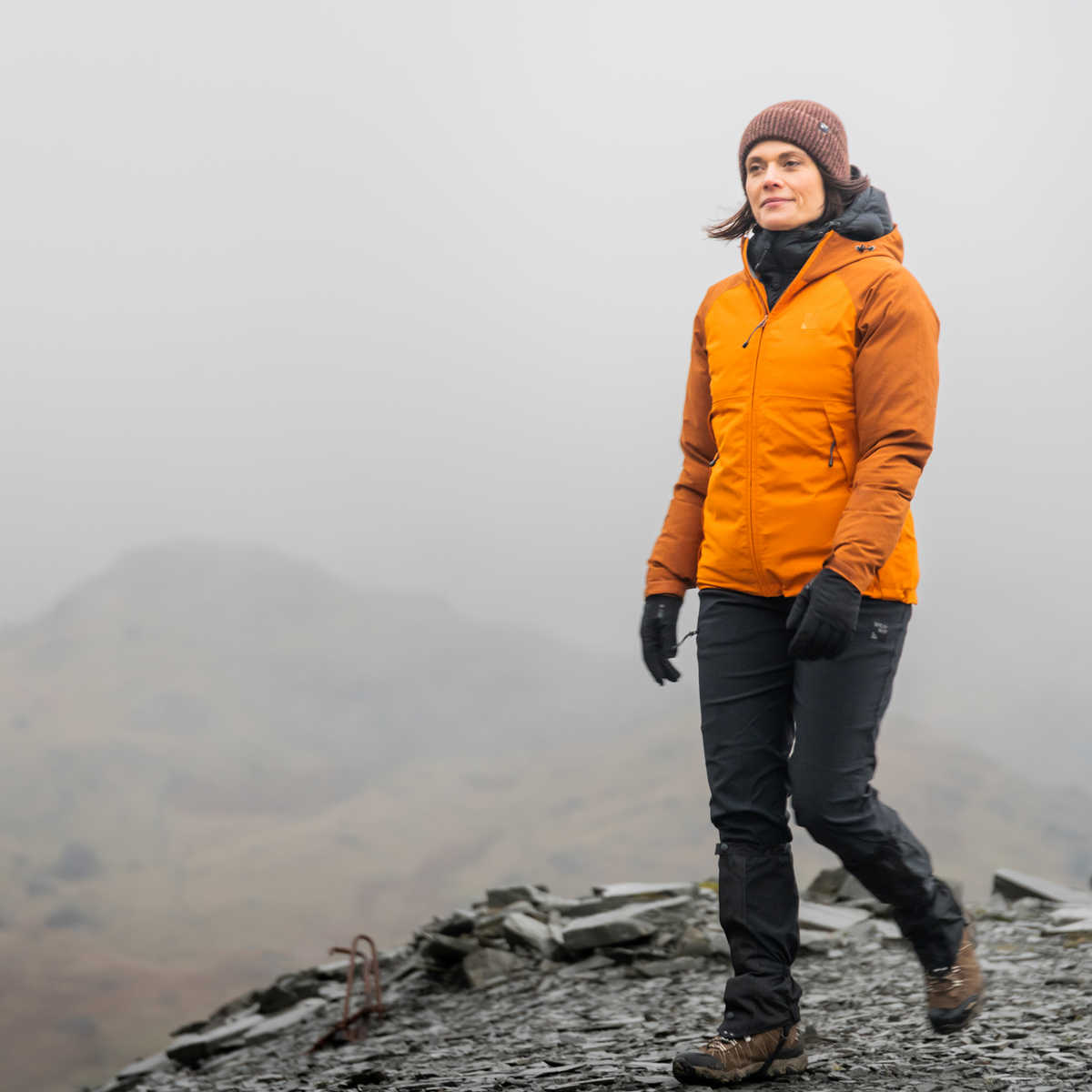 Person in an orange jacket and wearing Trekmates Women's Bala DRY Waterproof Gloves Black TM-008785 standing on a misty mountain landscape.
