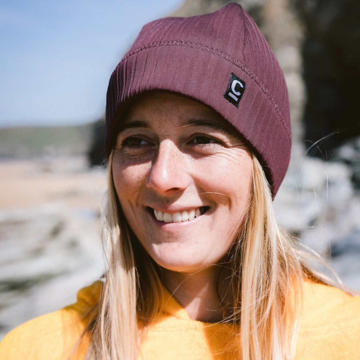 Woman wearing a C-Skins Unisex Storm Chaser Thermal Neoprene Swim Watersports Beanie Rust C-HOBE and an orange changing robe on a beach