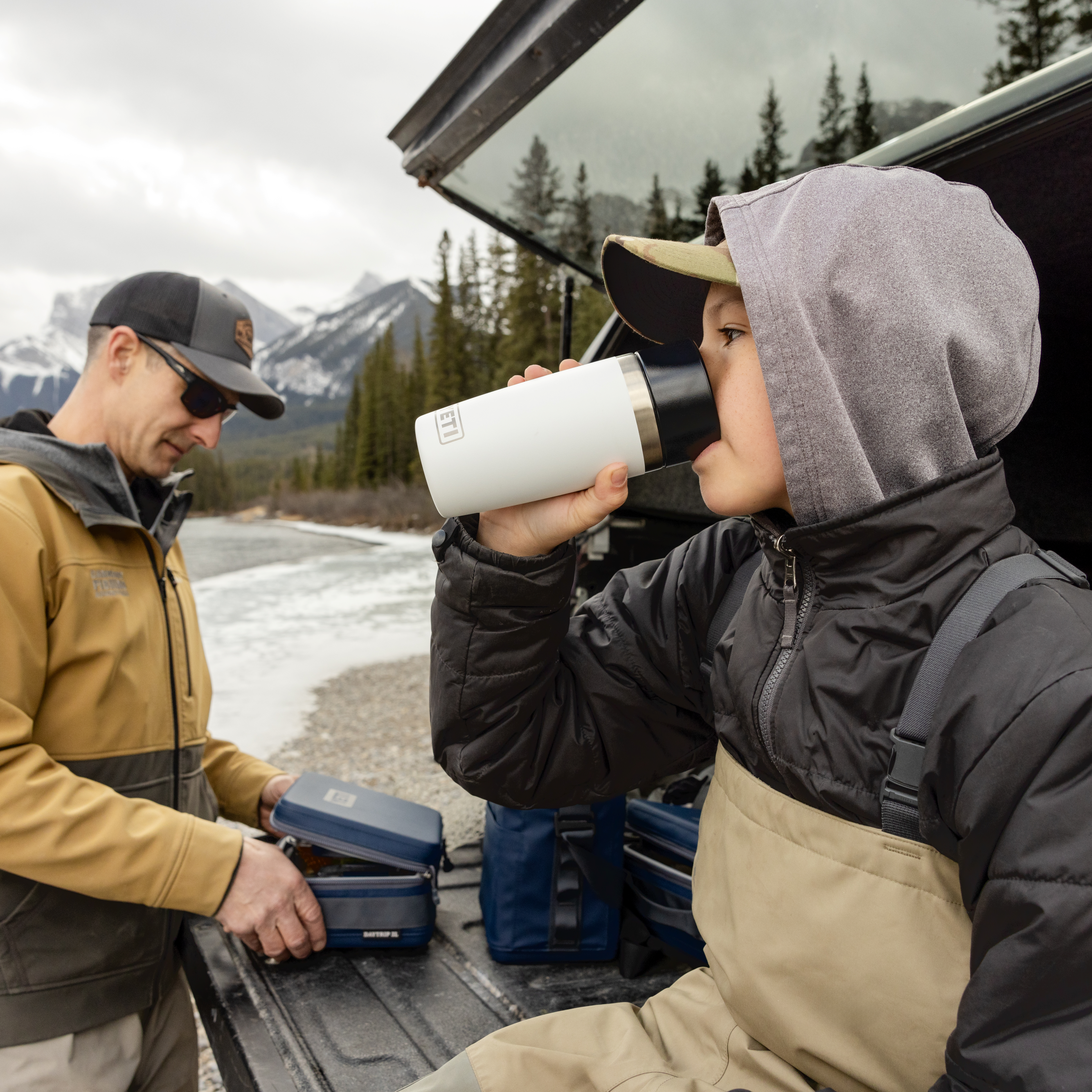 Young boy drinking out of a white Yeti travel bottle with commuter lid sitting in the boot of a car after fishing