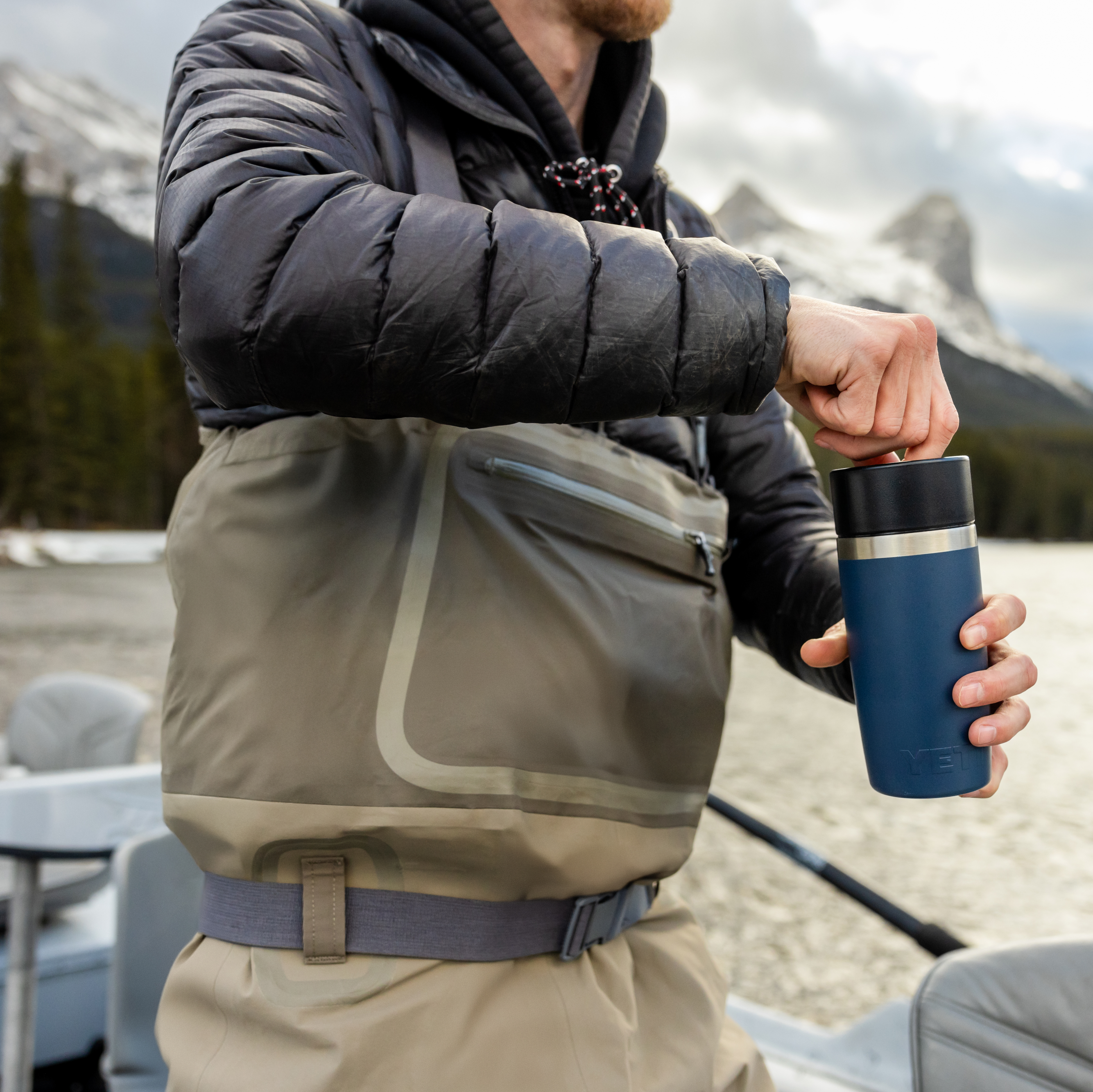Person holding a navy Yeti travel bottle with commuter lid on a fishing boat on a lake