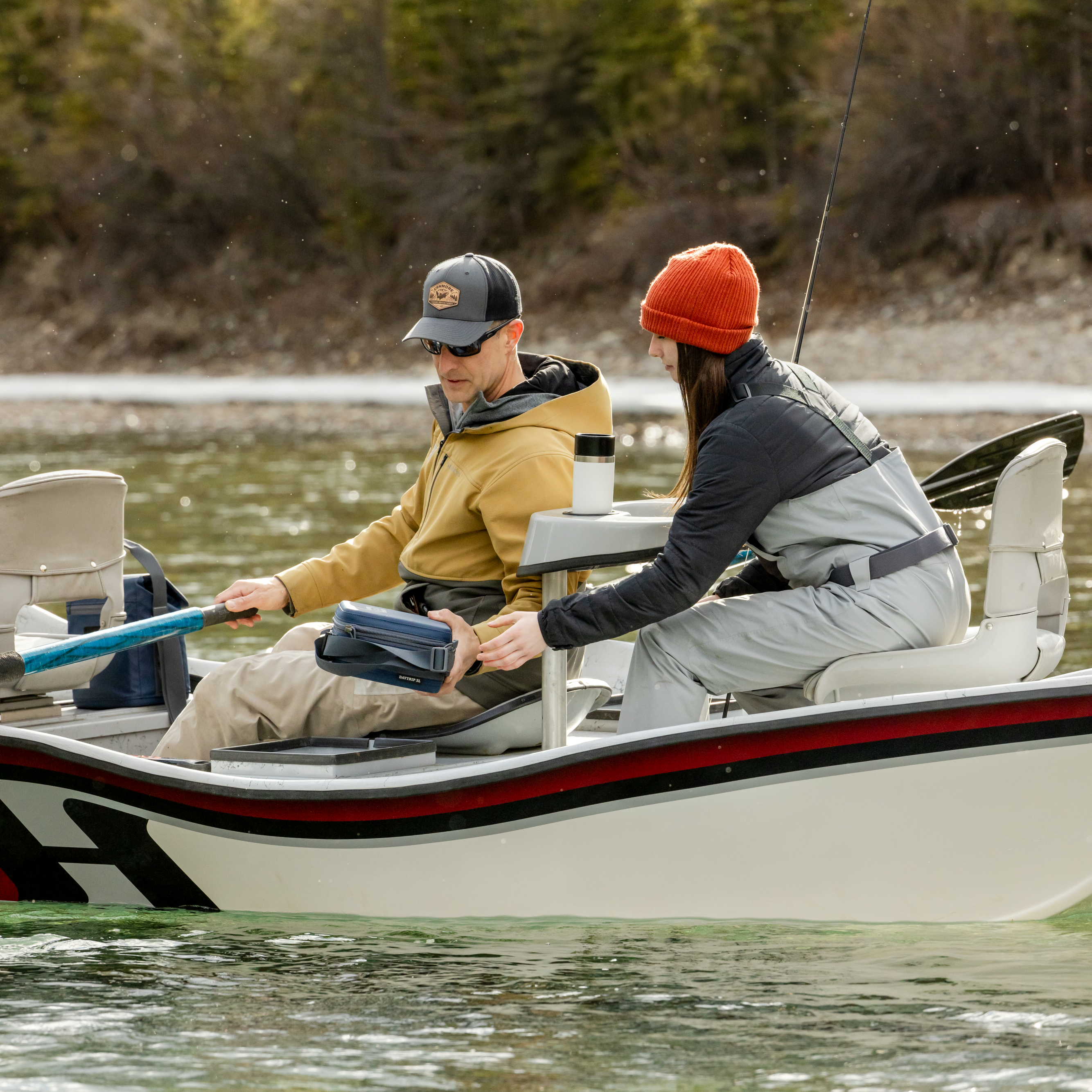 Young girl and her Dad fishing on a boat on a lake wearing waders. White Yeti travel bottle with commuter lid in the cupholder.