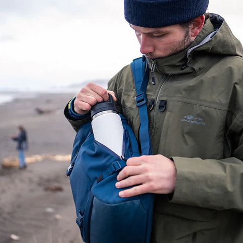 Man taking a white Yeti Rambler 26oz Chug Cap Bottle Yeti-Chug-26oz out of his bag on a moody beach