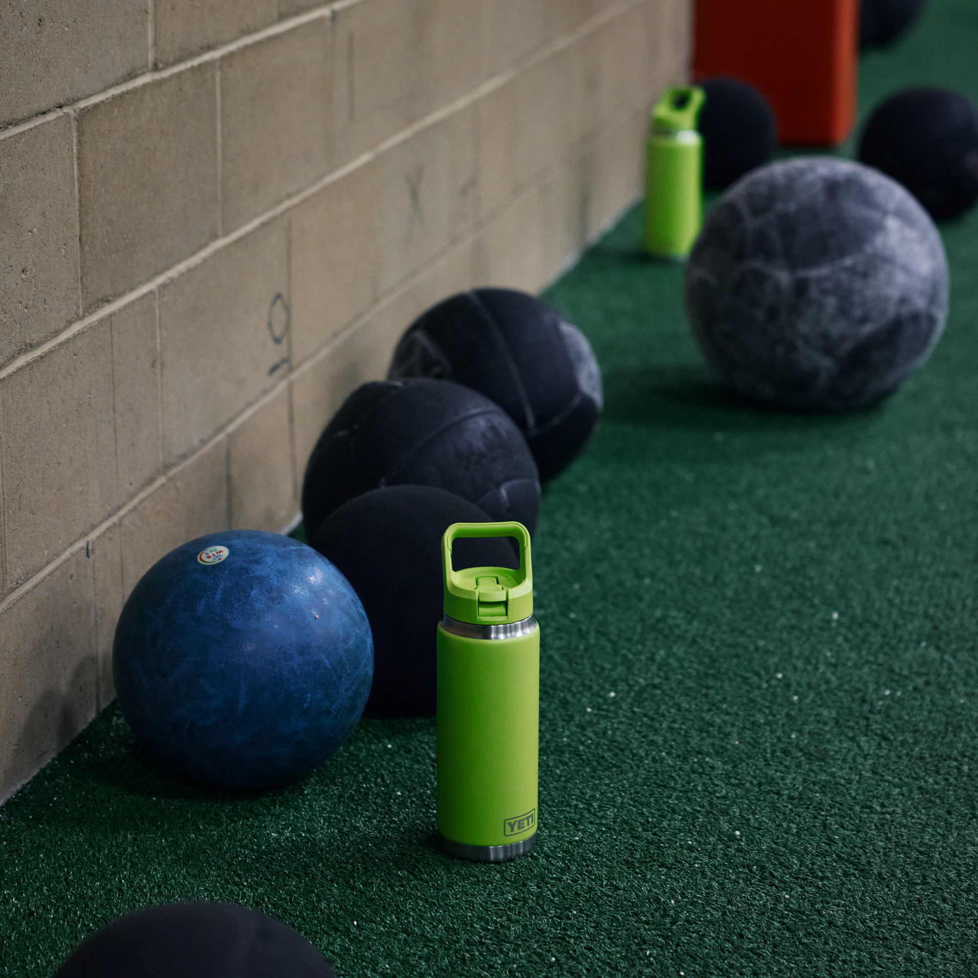 Yeti Rambler 26oz Straw Bottle Venom Yeti-RamblerStraw-26oz 70000005999 and black exercise balls on a green floor against a beige brick wall.