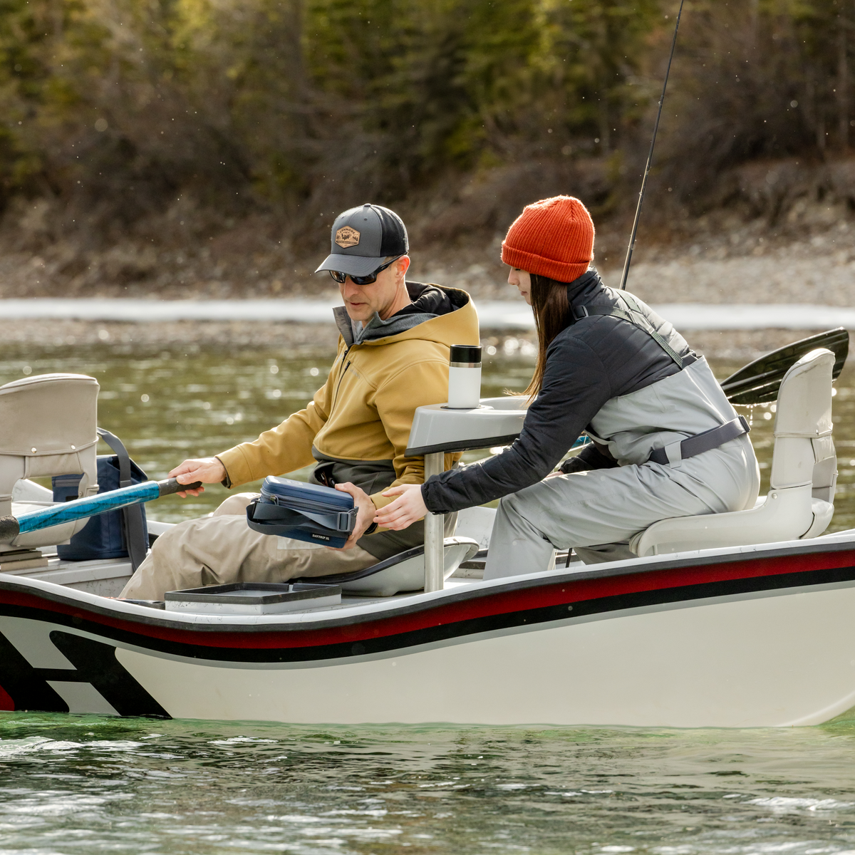 Two people fishing in a boat on a lake with trees in the background yeti travel mug in the cup holder