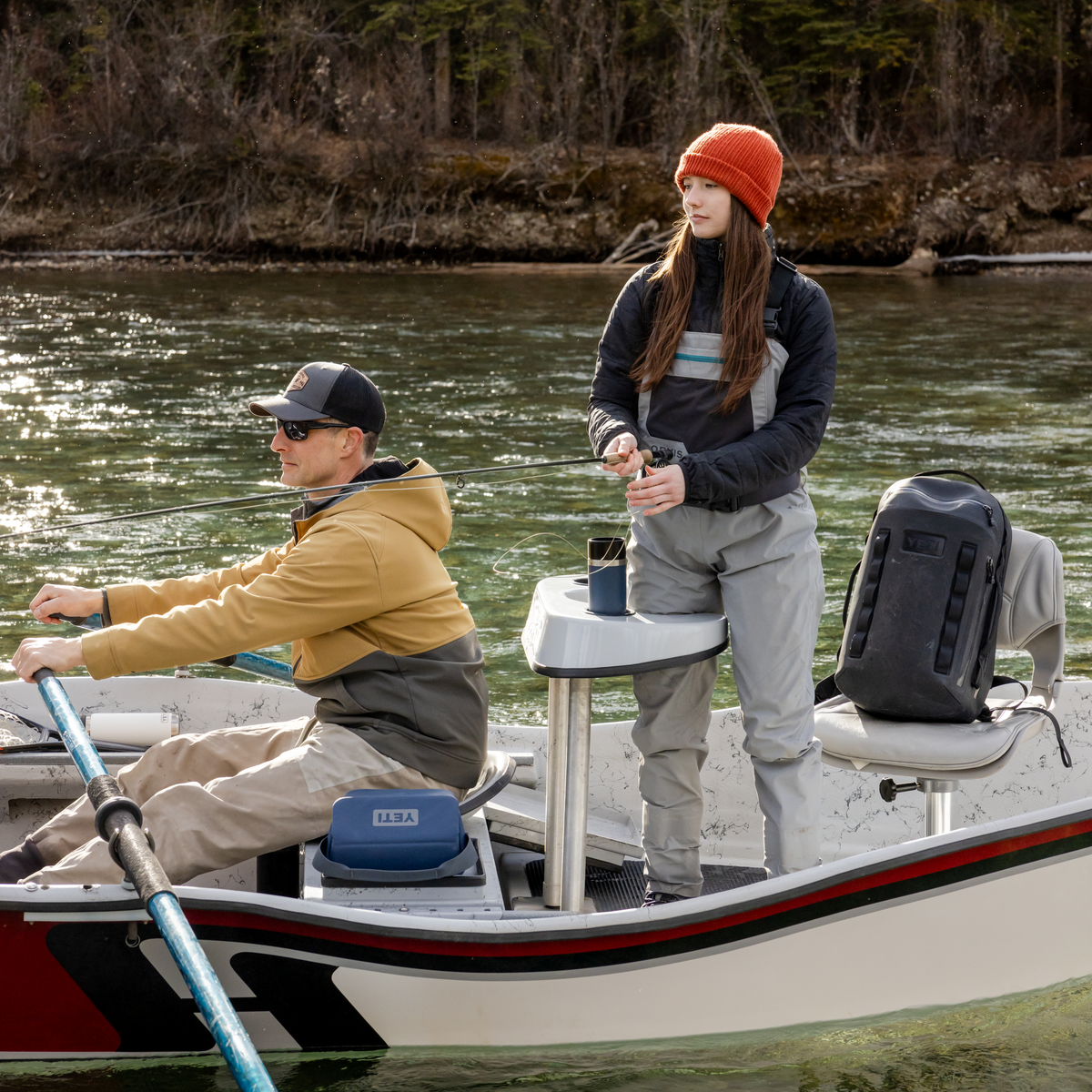 Two people on a boat in a body of water with trees in the background and a Yeti rambler travel mug in the cupholder