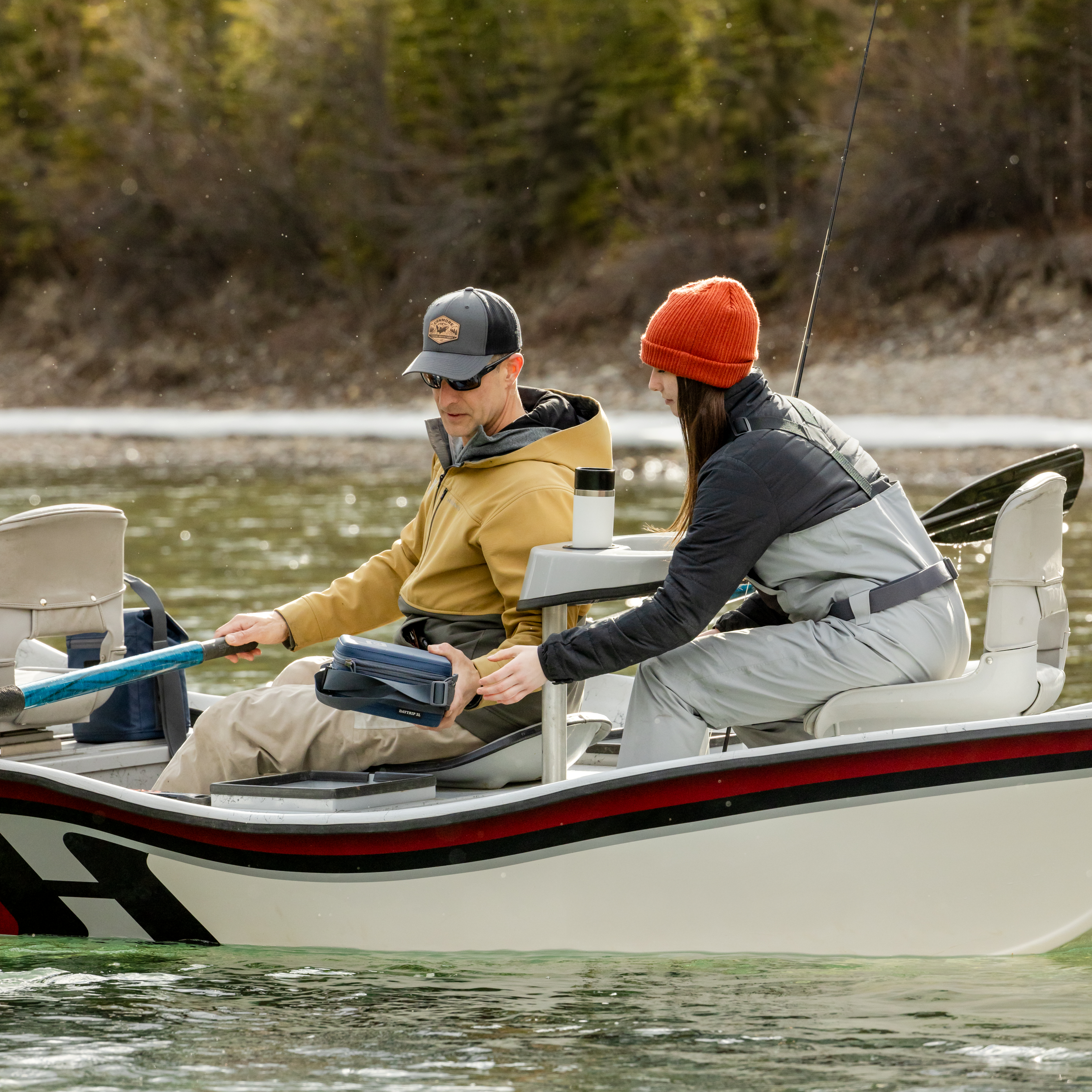 Two people fishing in a boat on a lake with trees in the background. Yeti rambler insulated travel mug in the cupholder.
