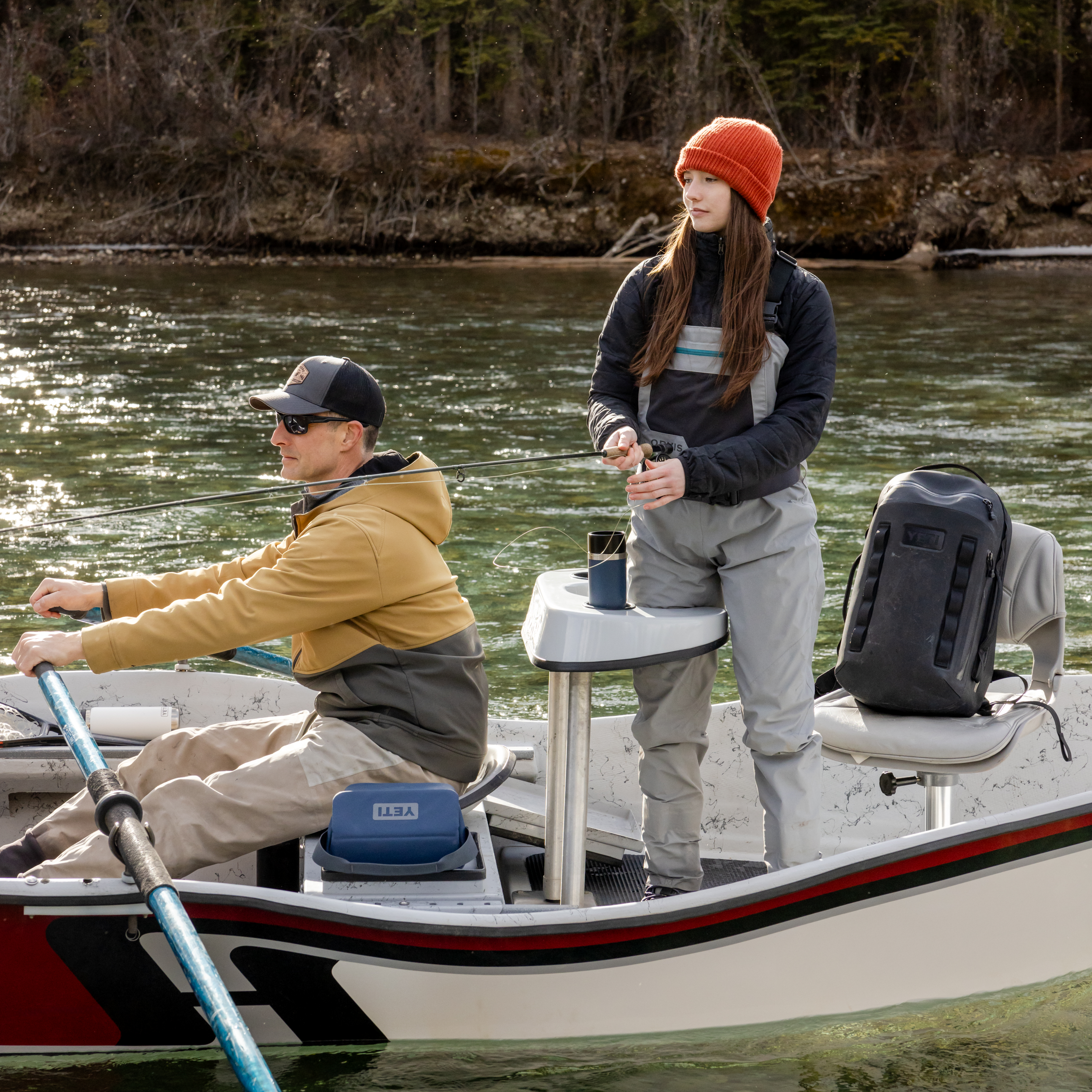 Two people on a boat in a body of water with trees in the background with a Yeti rambler travel mug in the cupholder