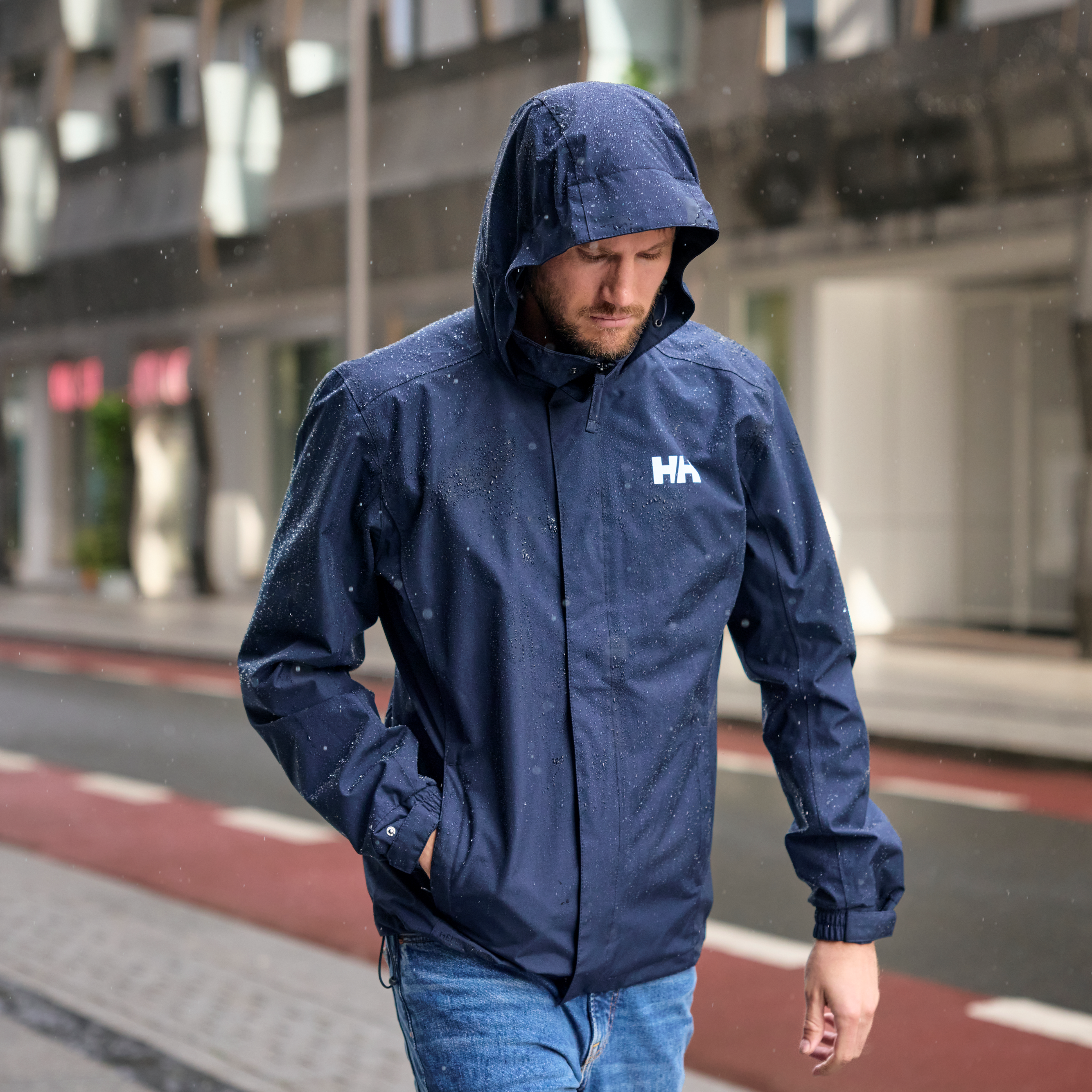 Man walking in a city in the rain wearing 62643 Helly Hansen Men's Dubliner Waterproof Rain Jacket Navy 597 with water droplets on the jacket