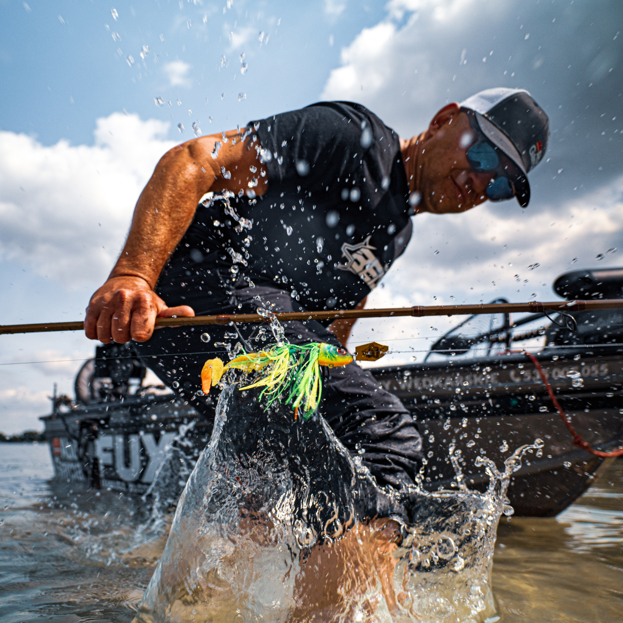 Man in the water with an Abu Garcia Beast Bladed Jig 25cm 50g Soft Lure Firetiger 4 Pack 162119 on his rod. Water splashing around him and boat in the background.