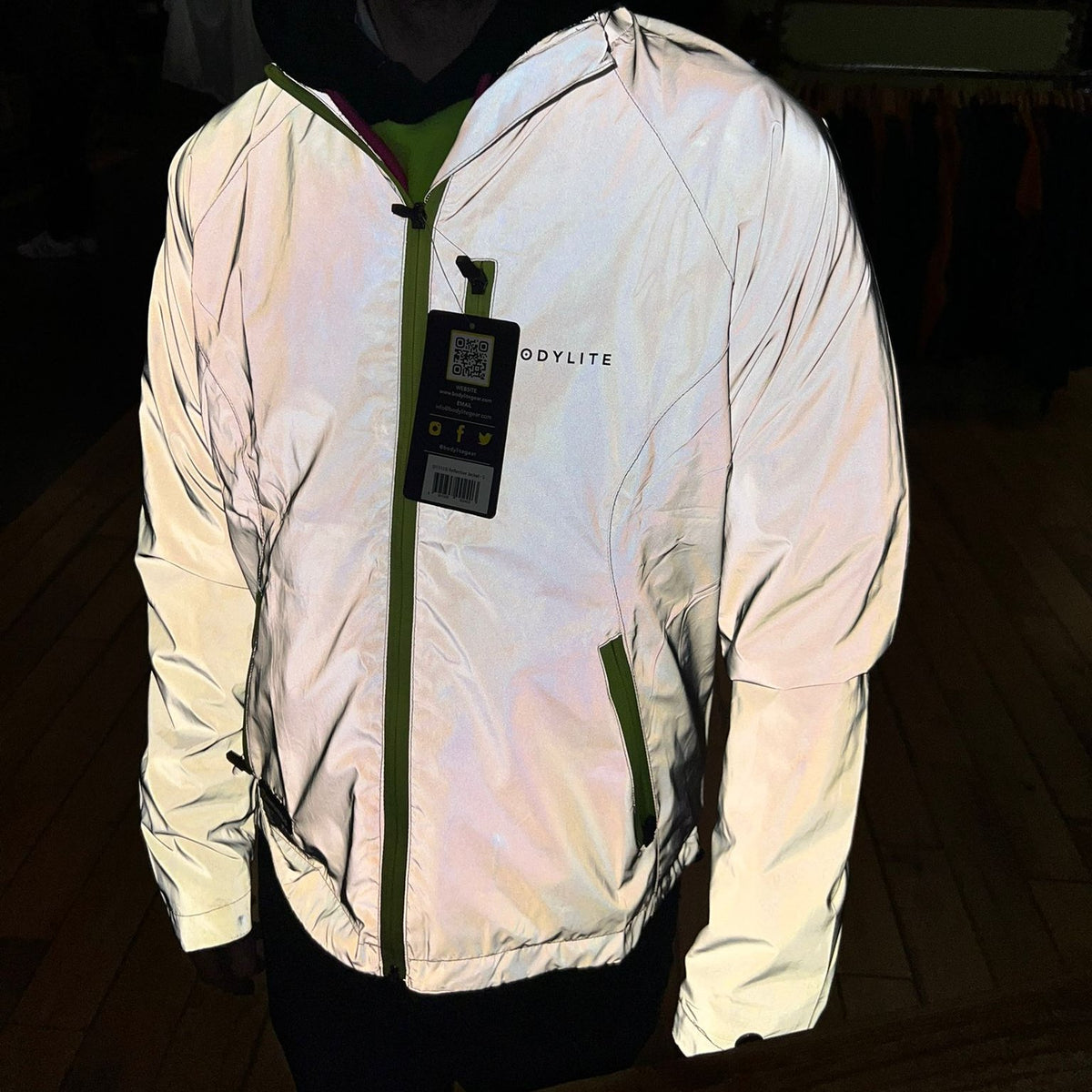 A person wearing a Bodylite Unisex Fully Reflective Jacket 01303-ALL SIZES, standing in a dark indoor setting.