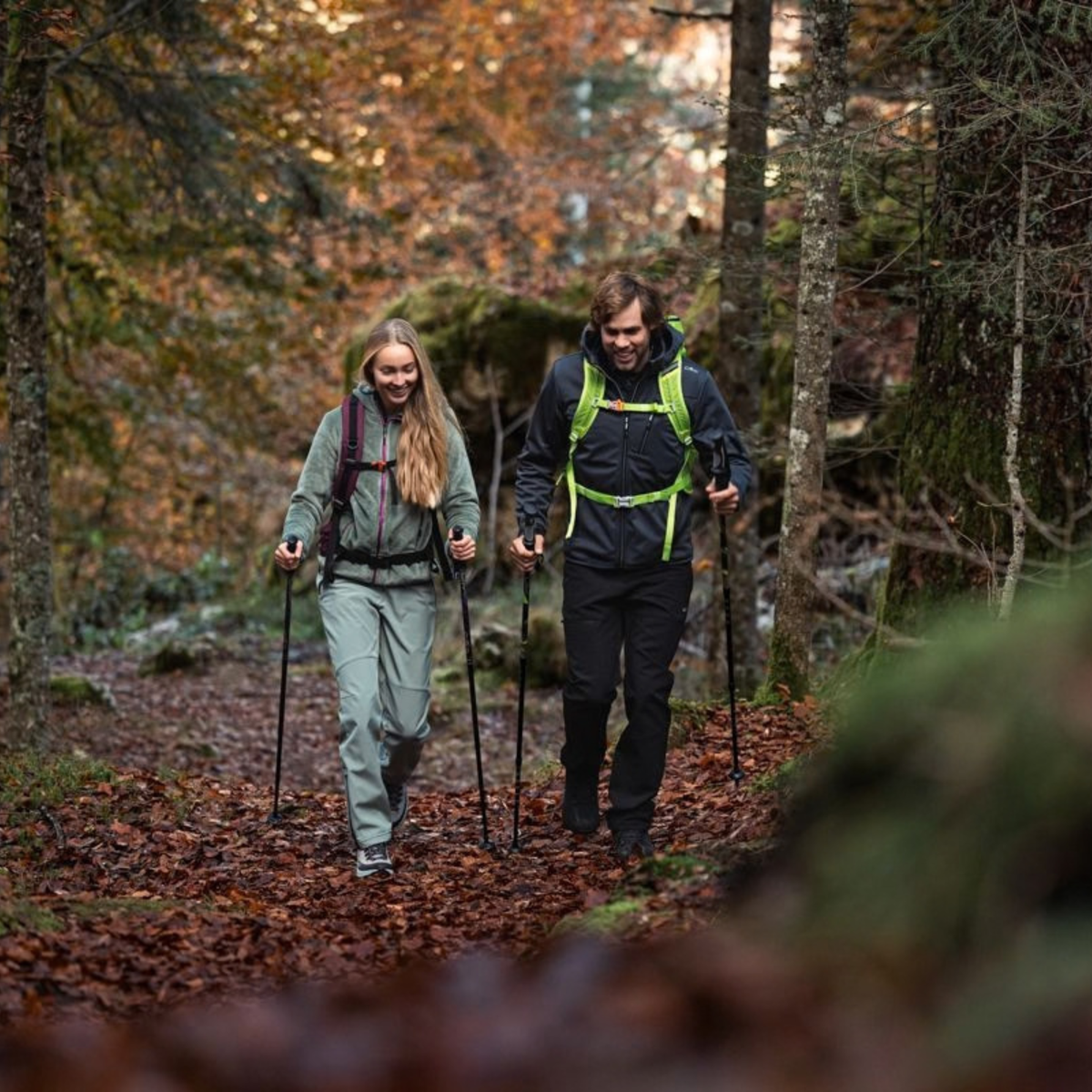 Two people hiking in a forest using hiking poles, wearing backpacks and other outdoor apparel. Woman wearing CMP Laredo Trekking Daypack 22L C910 Amaranto 3V17957
