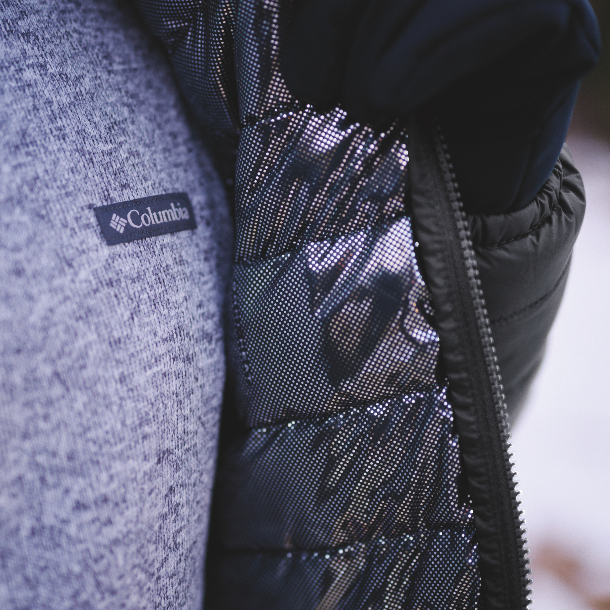 Close-up of a Columbia Men's Powder Lite II Insulated Jacket Black 010 2086964 lining, shown next to a grey knit fleece with a Columbia logo patch
