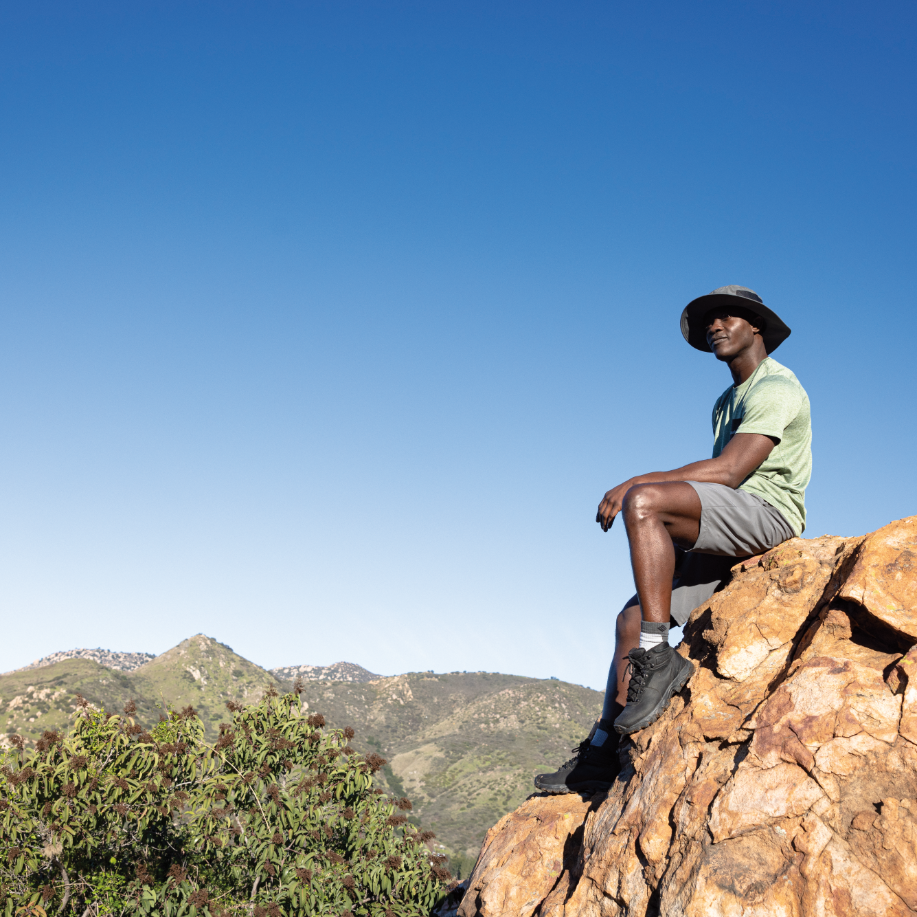 Person sitting on a rock with mountains and clear blue sky in the background wearing Columbia Unisex Bora Bora UPF50 Booney Sun Hat Grill 028 1447091