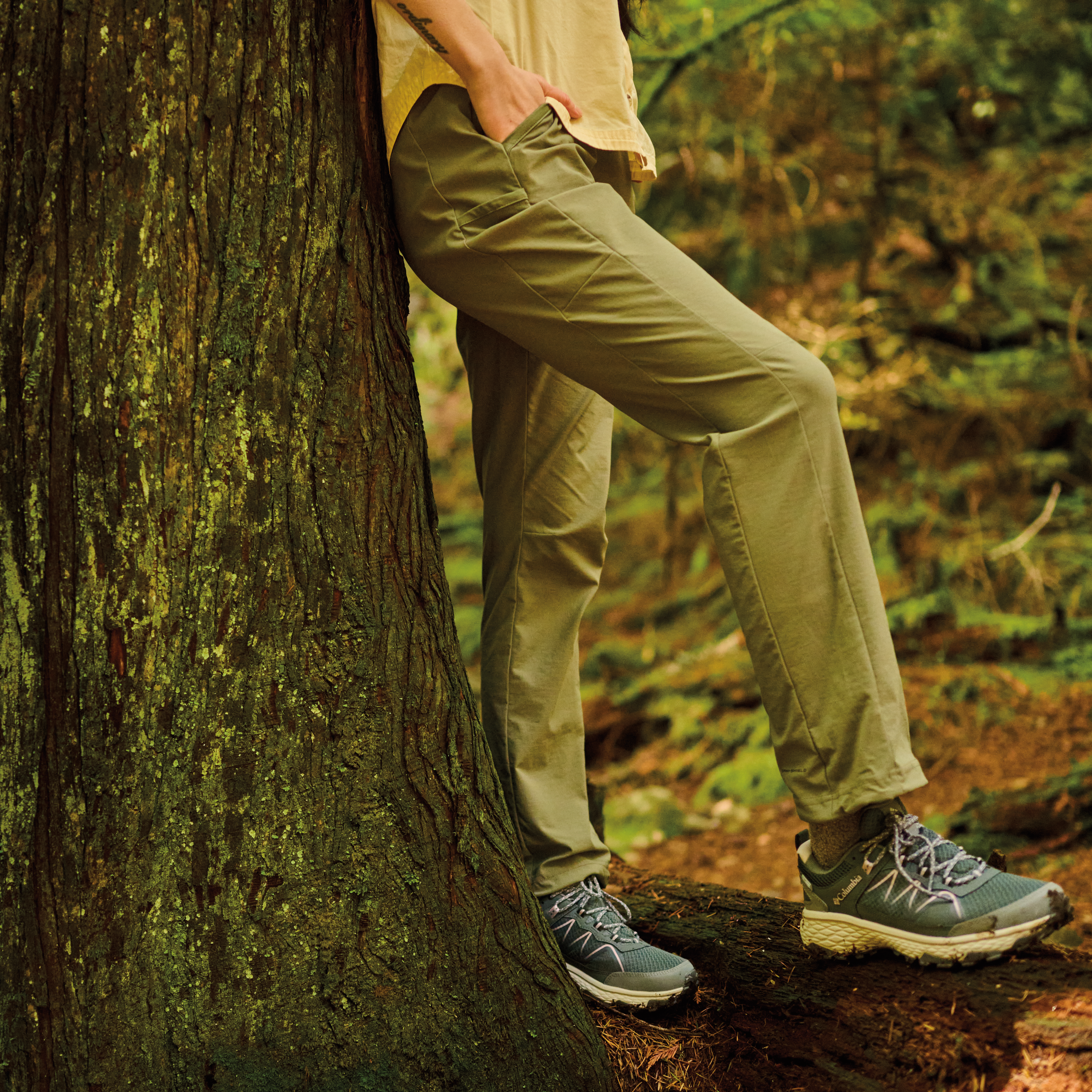 Woman wearing Columbia Women's Peakfreak Rush Outdry Waterproof Trail Shoes Grill Vapor 028 2108431 resting against a tree in the forest