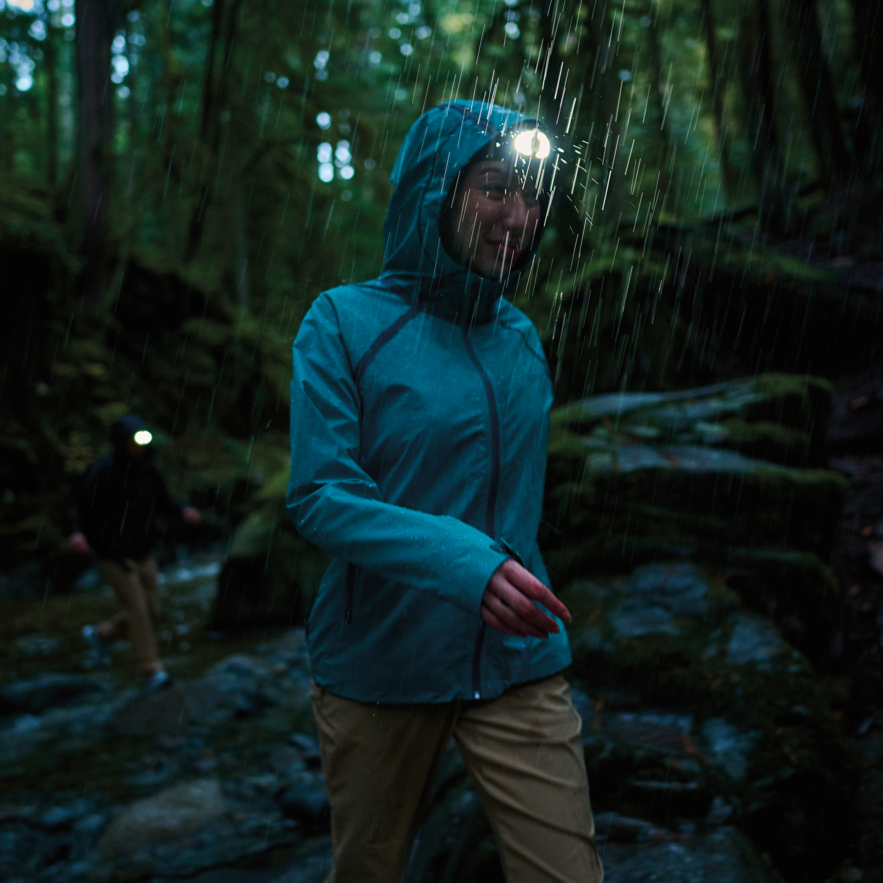 Woman hiking in a dark forest, in the rain, wearing a Columbia Women's Reign No Shine Outdry Extreme Waterproof Jacket River Blue 364 2116293